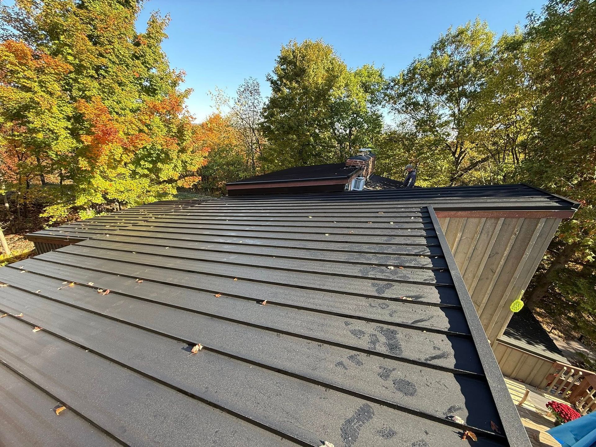 Rooftop with dark shingles and a vent, surrounded by autumn trees under a clear sky