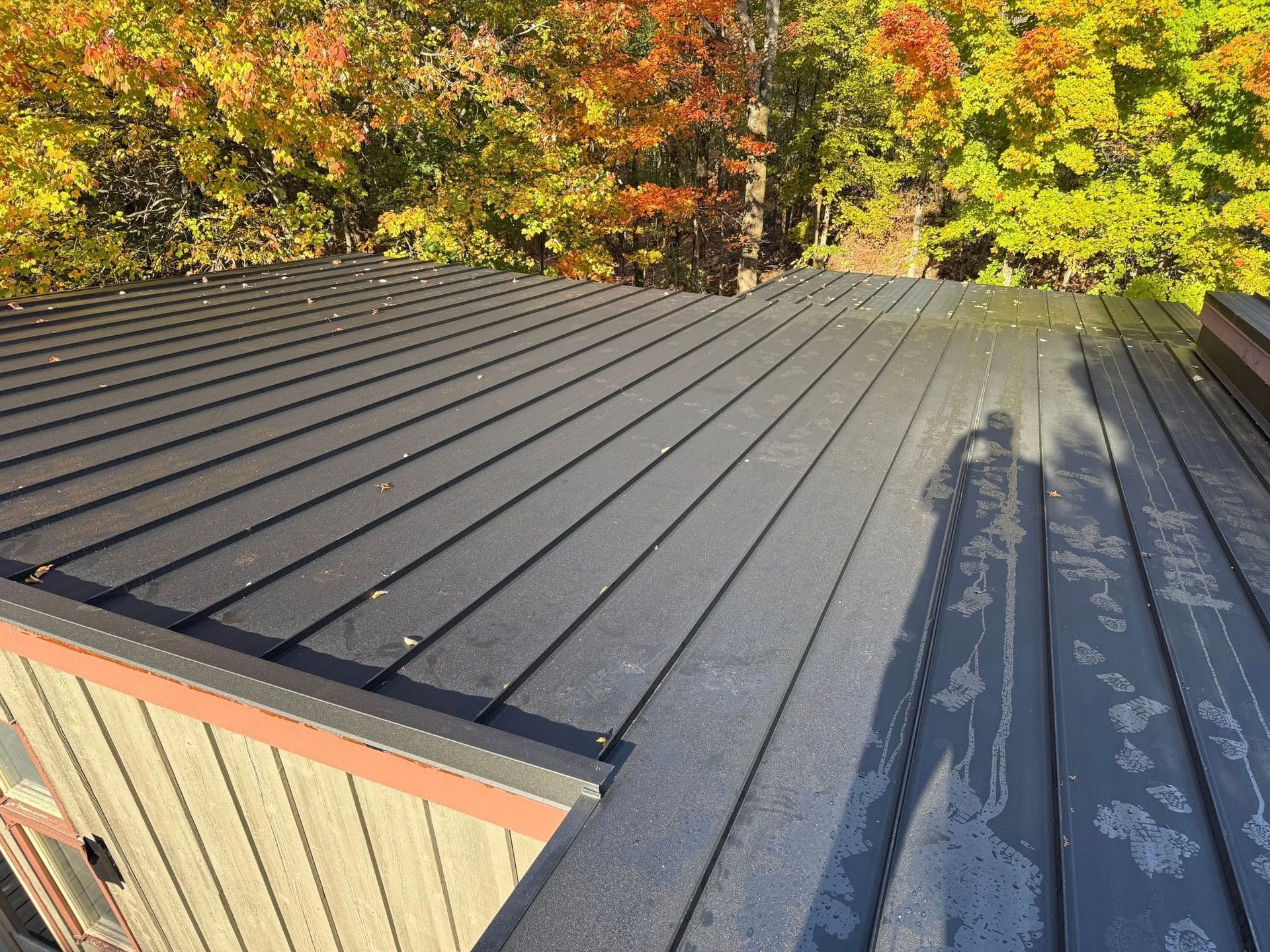 Black metal roof with long shadows, bordered by autumn trees in yellow, orange, and green.