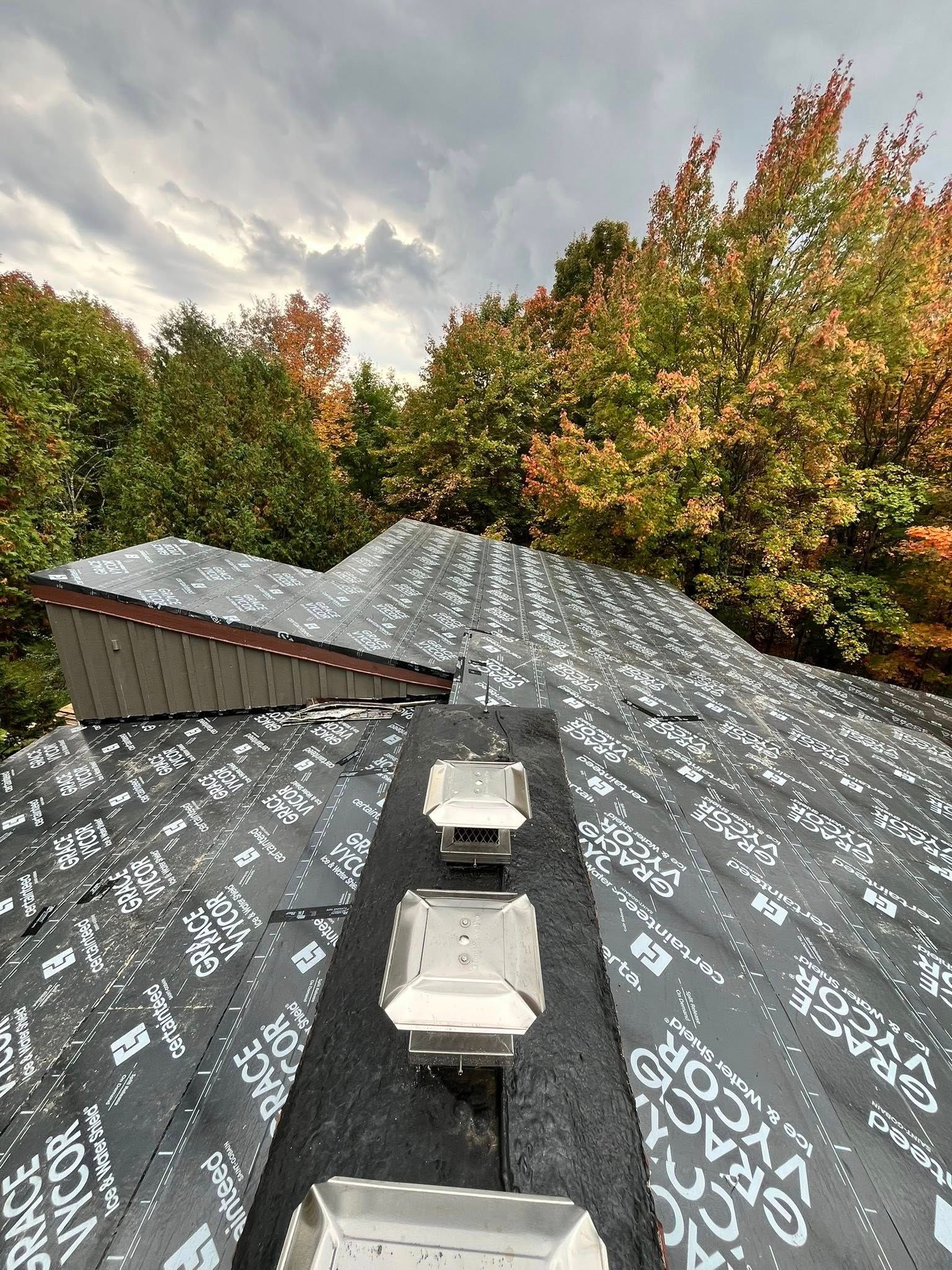 Rooftop with two vents under a cloudy sky, framed by autumn trees