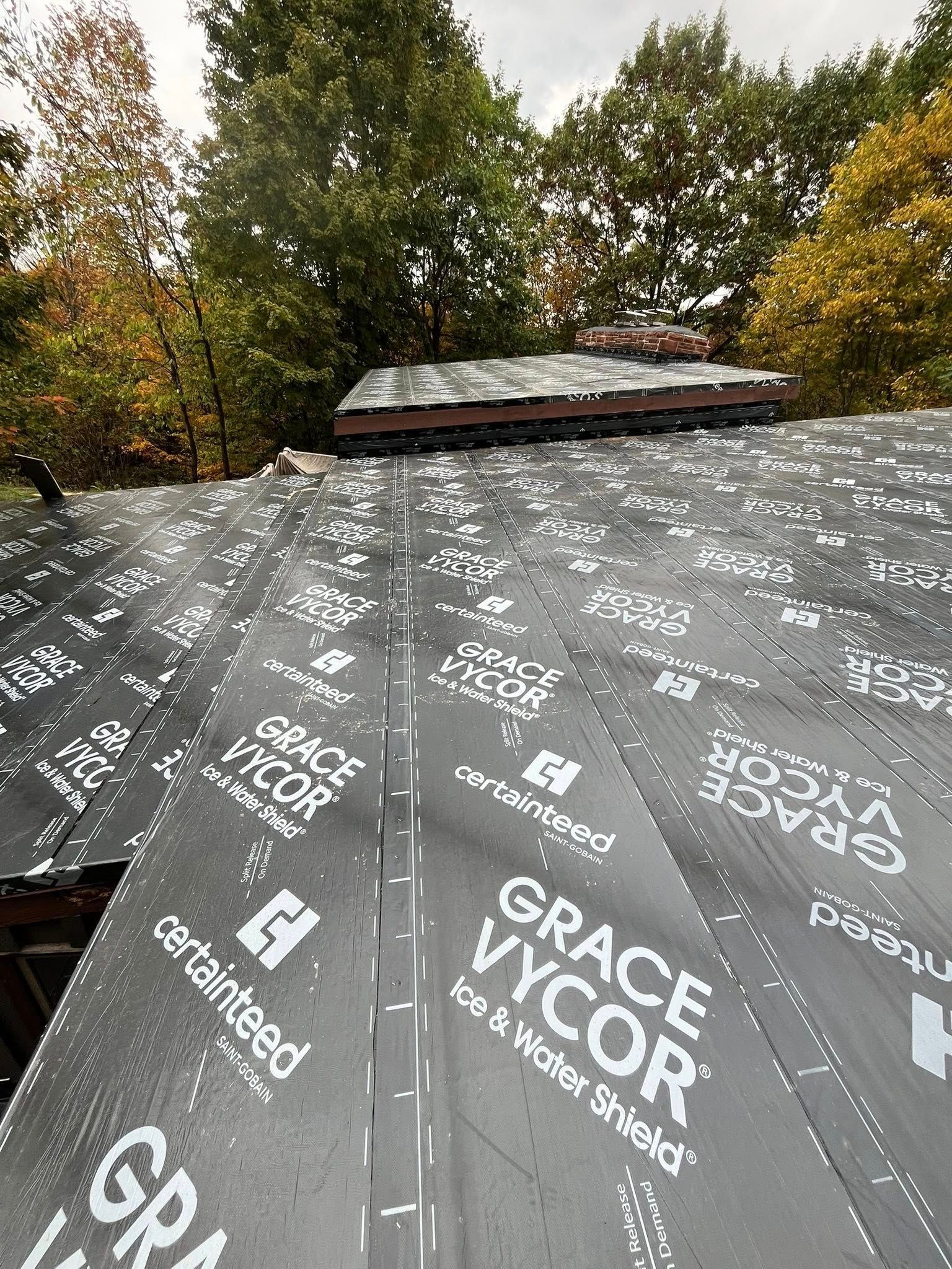 Roof under construction with black GRACE Vycor underlayment and trees in the background