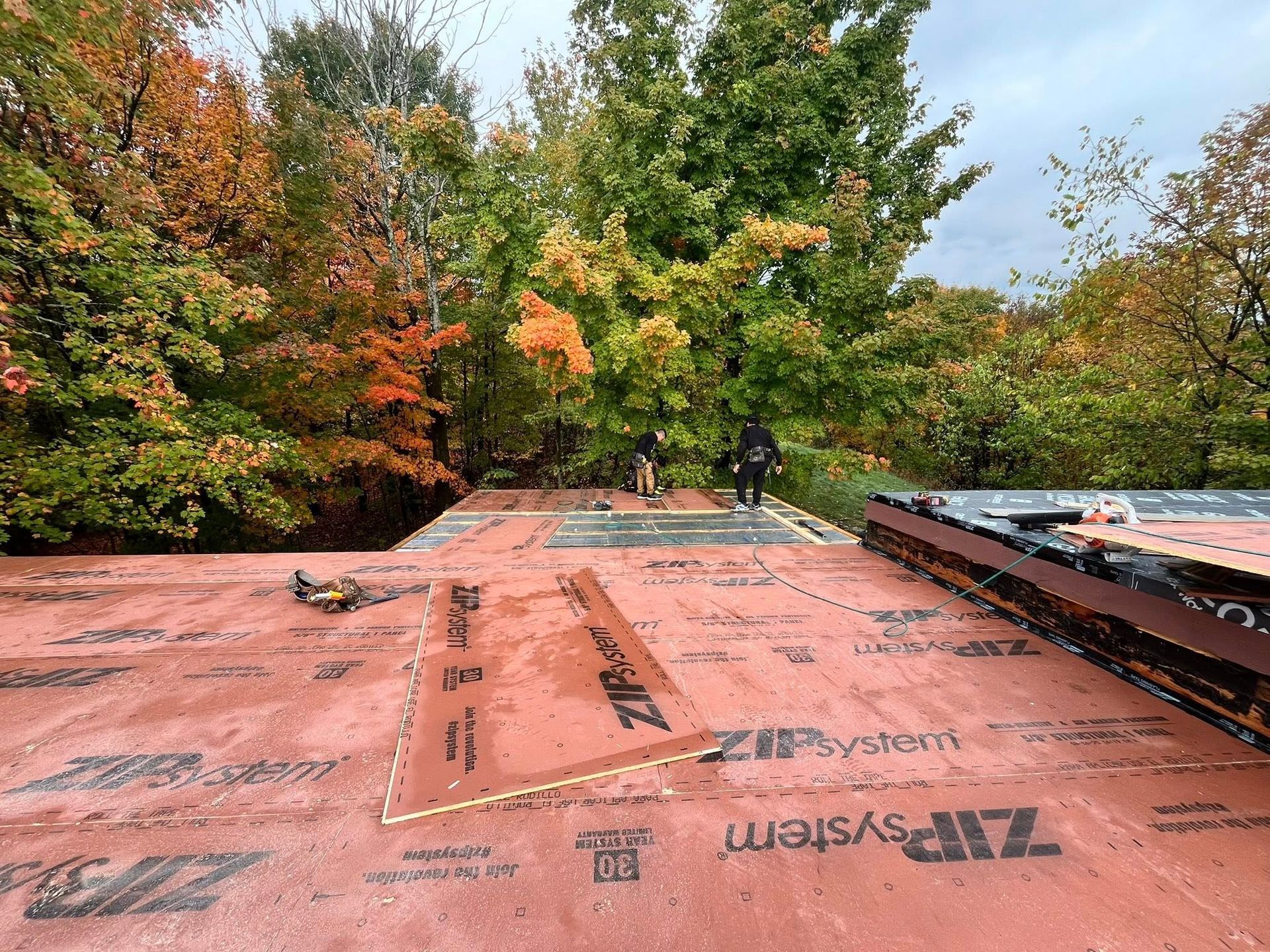 Rooftop underlayment with tools, bordered by fall trees and two workers in the distance