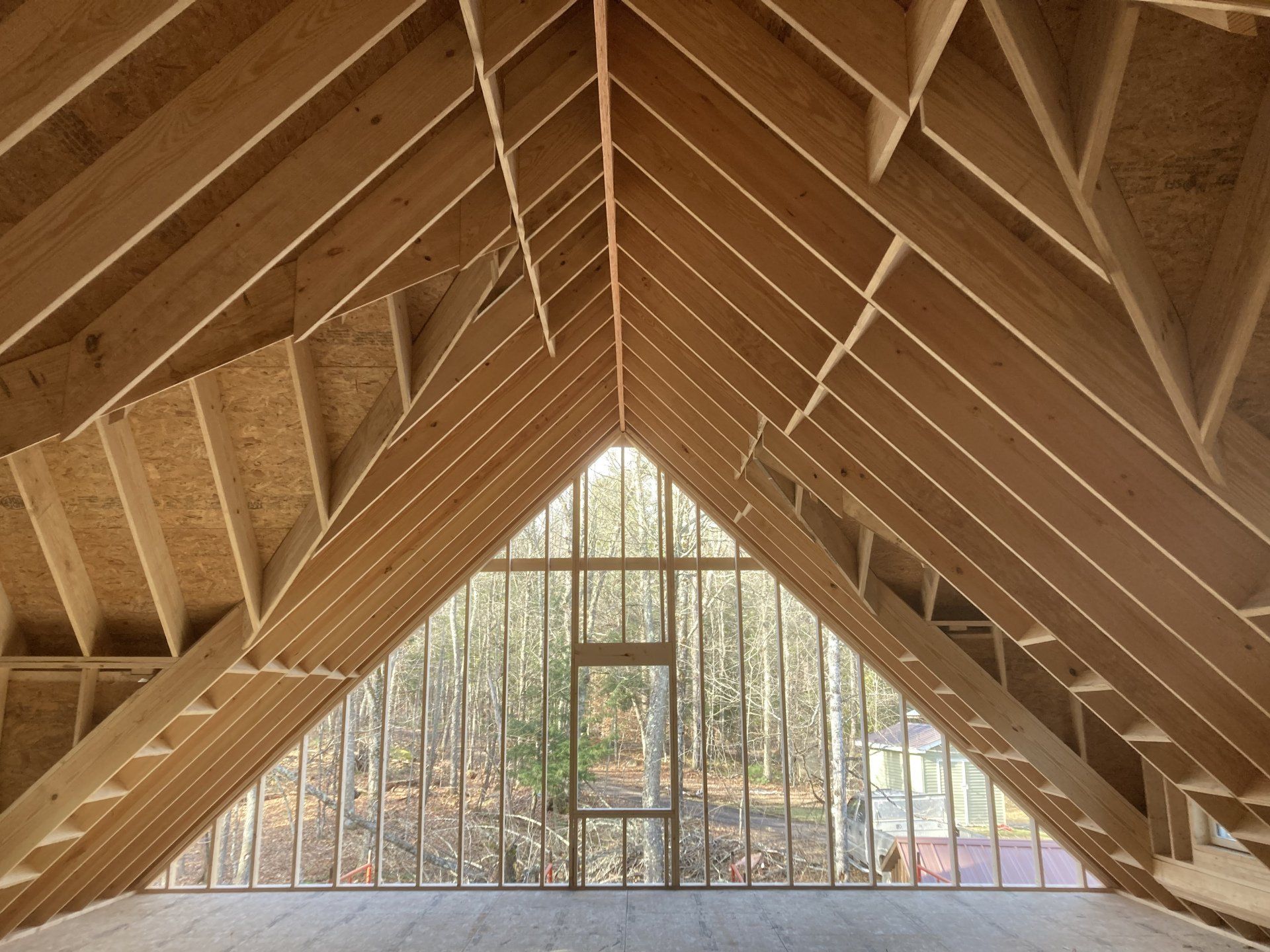 Interior of an unfinished wooden A-frame cabin with exposed rafters and a large triangular window.