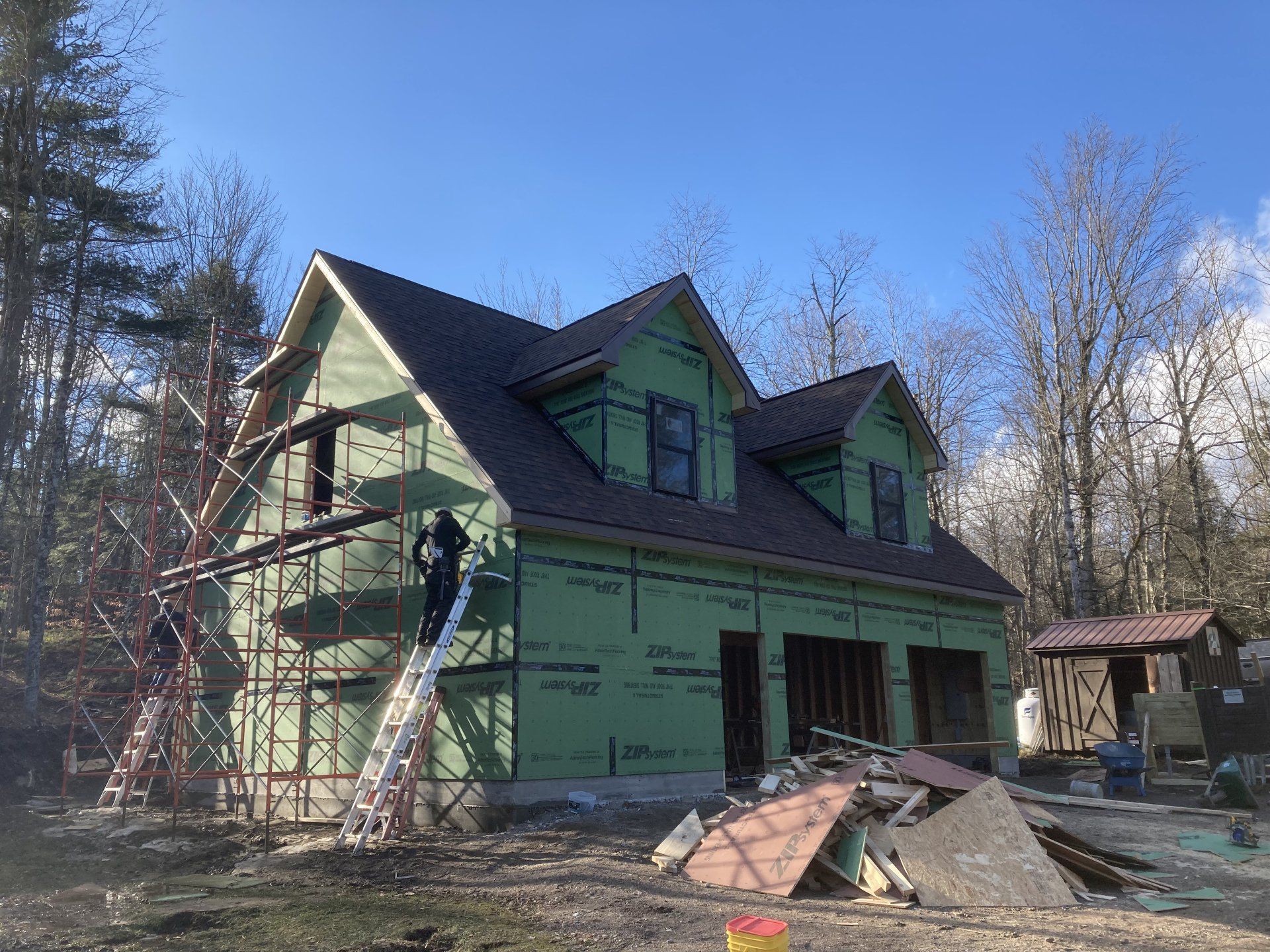 Green house under construction with workers on ladders and scaffolding, debris in front yard