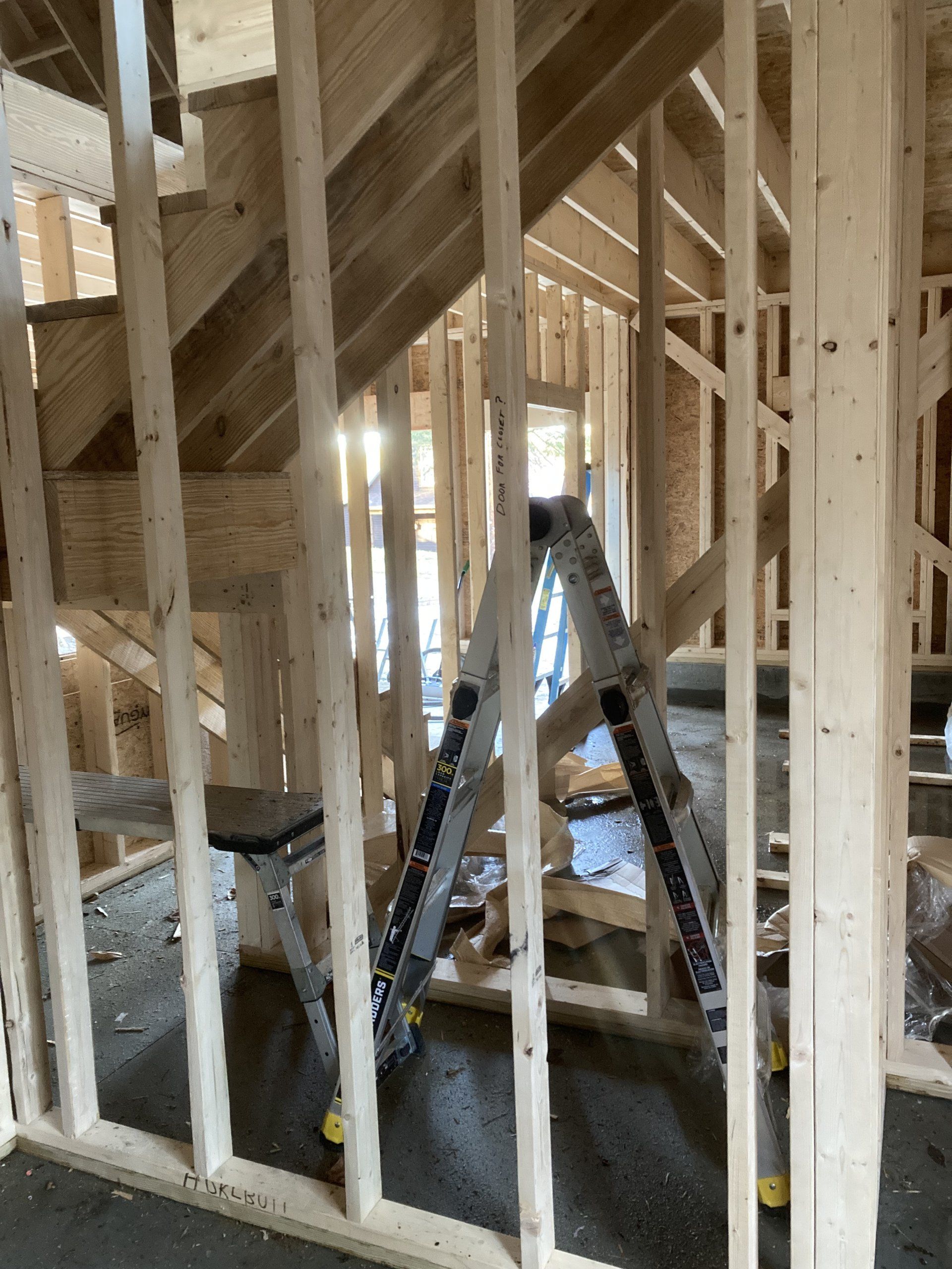 Framed interior of a house under construction with ladders and exposed wooden studs in the stairwell.