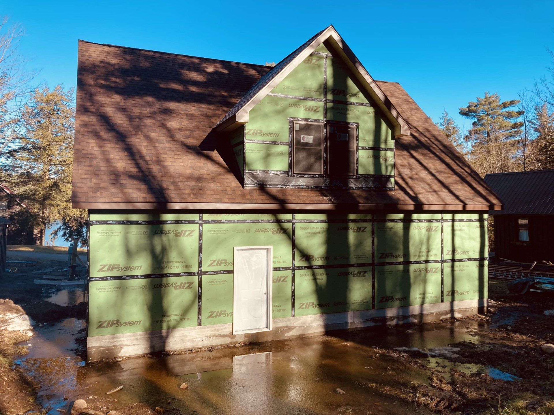 Green house with a steep brown roof and white door, seen in muddy water under a clear blue sky.