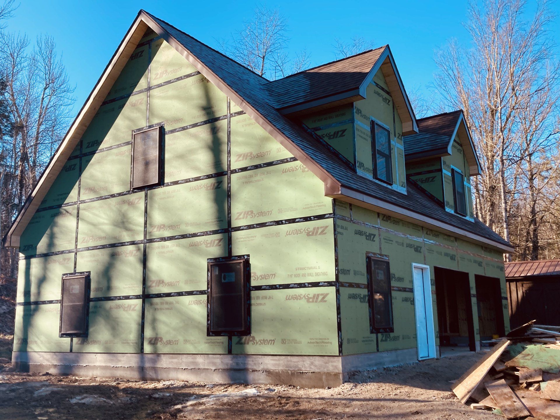 Partially renovated two-story house with pale green siding, dark trim, and boarded windows under a clear blue sky