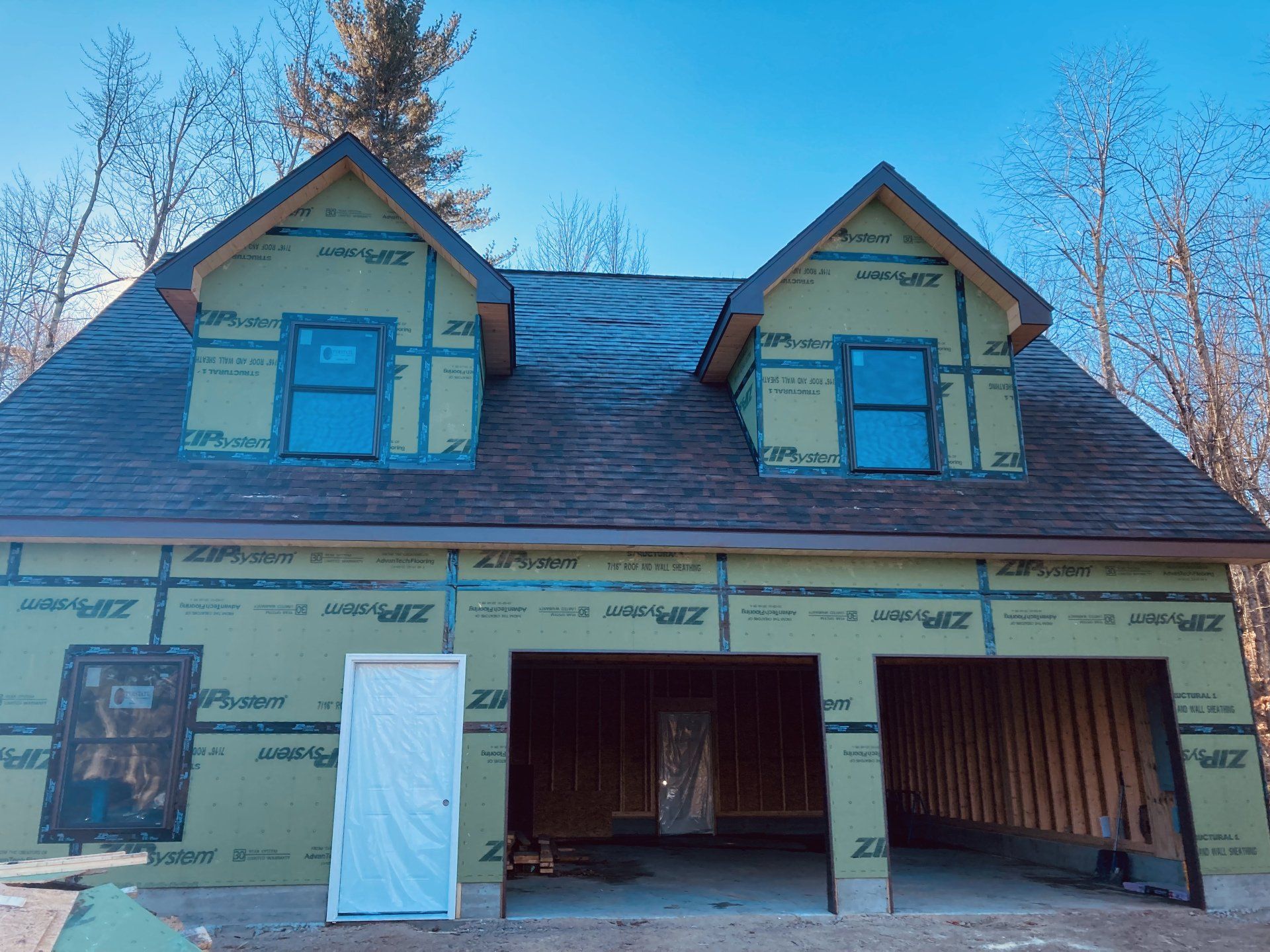 Partially built yellow house with blue-trimmed dormer windows and open garage under construction