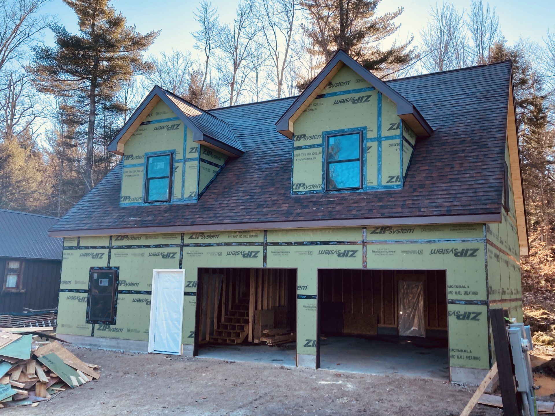 Partially built yellow house with blue dormers and an open garage under construction