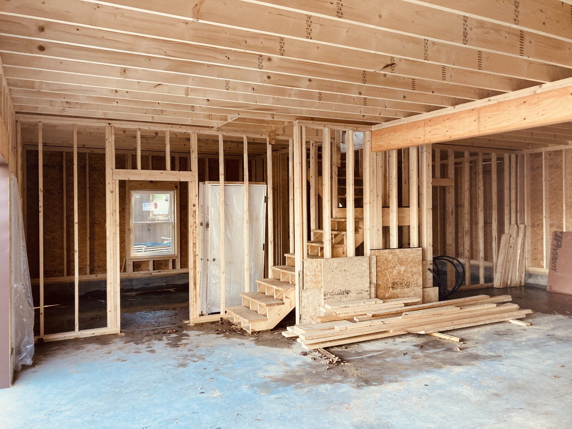 Interior of a house under construction with exposed framing, unfinished walls, and stacks of lumber on the floor