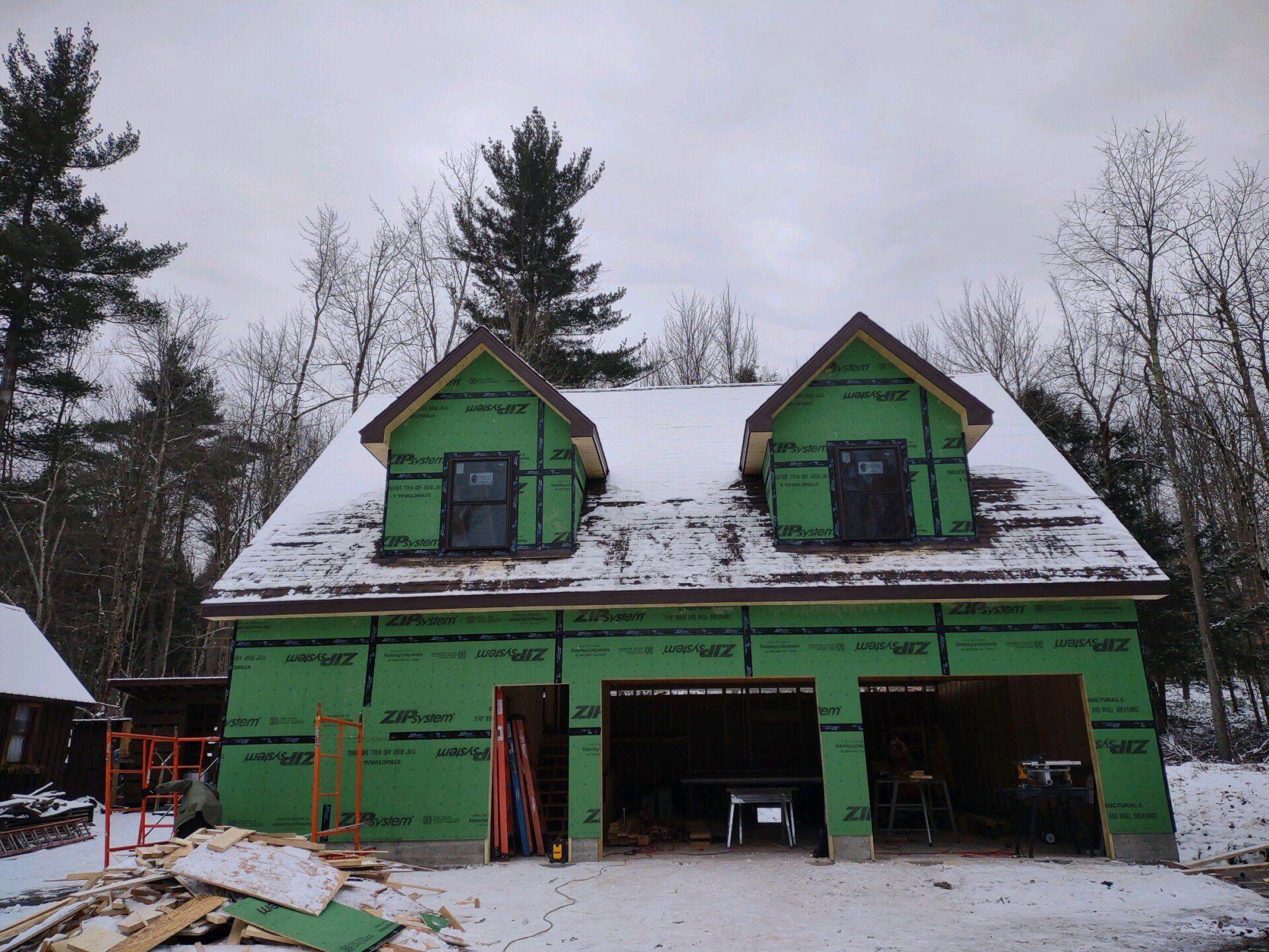 Green house under construction with snow on the roof and unfinished garage openings