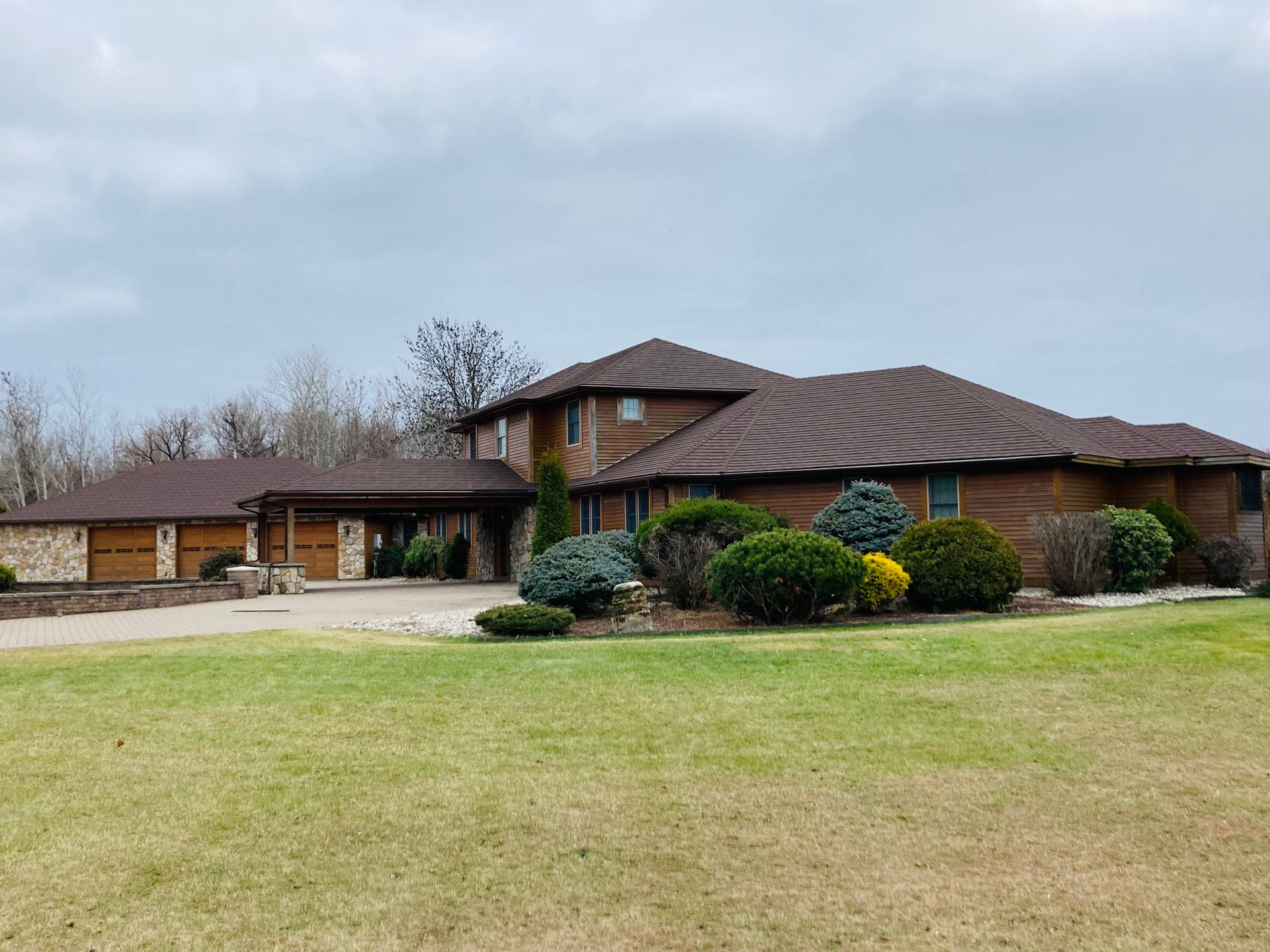 A large brick house with a brown roof is sitting on top of a lush green field.