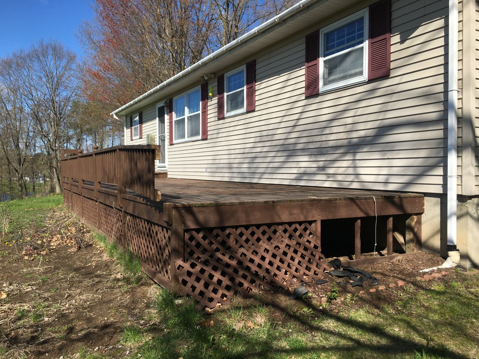 House exterior with beige siding, red shutters, and a long wooden deck with lattice skirting.