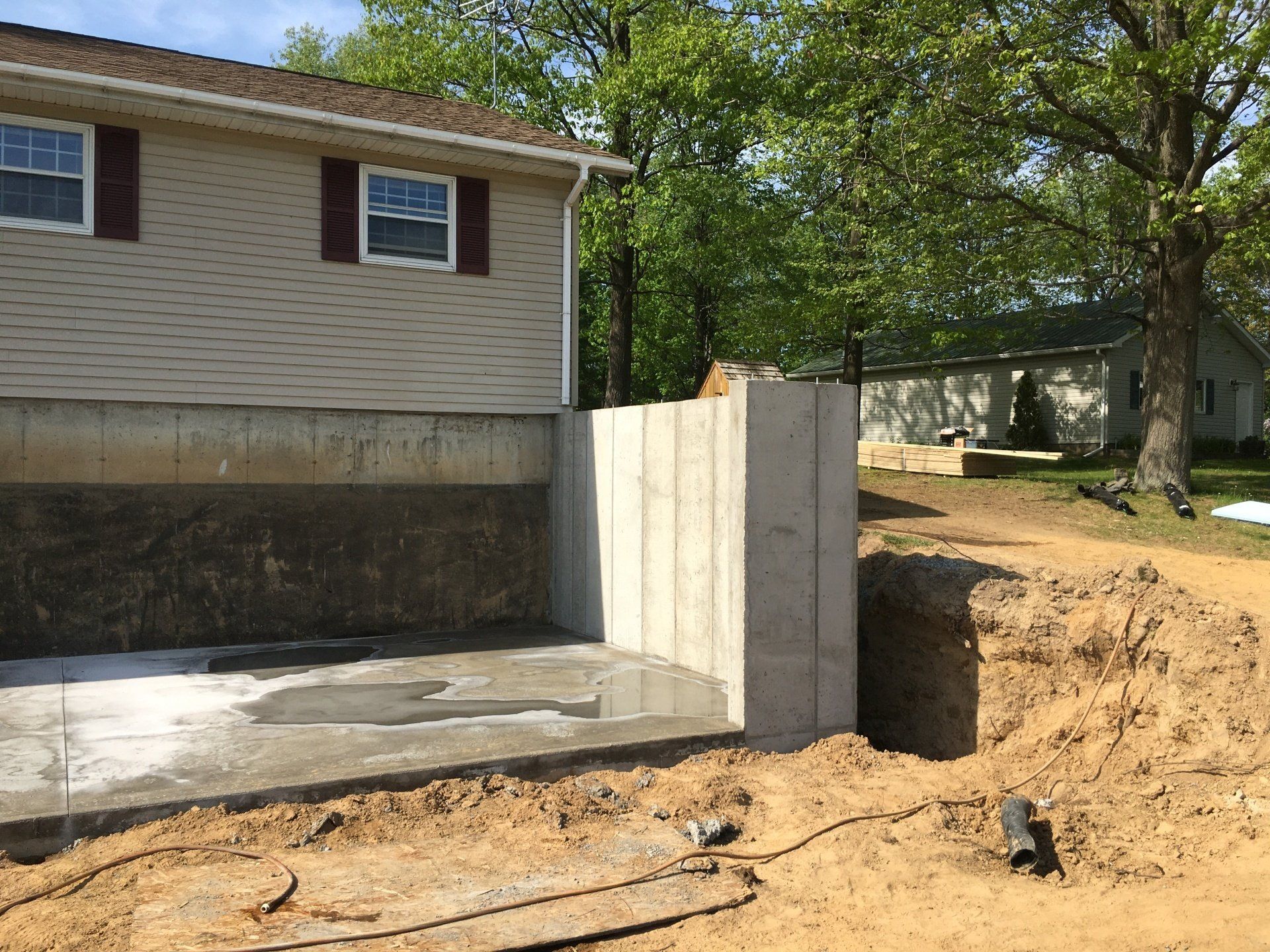 New concrete foundation wall beside a house under construction, with excavated dirt around it