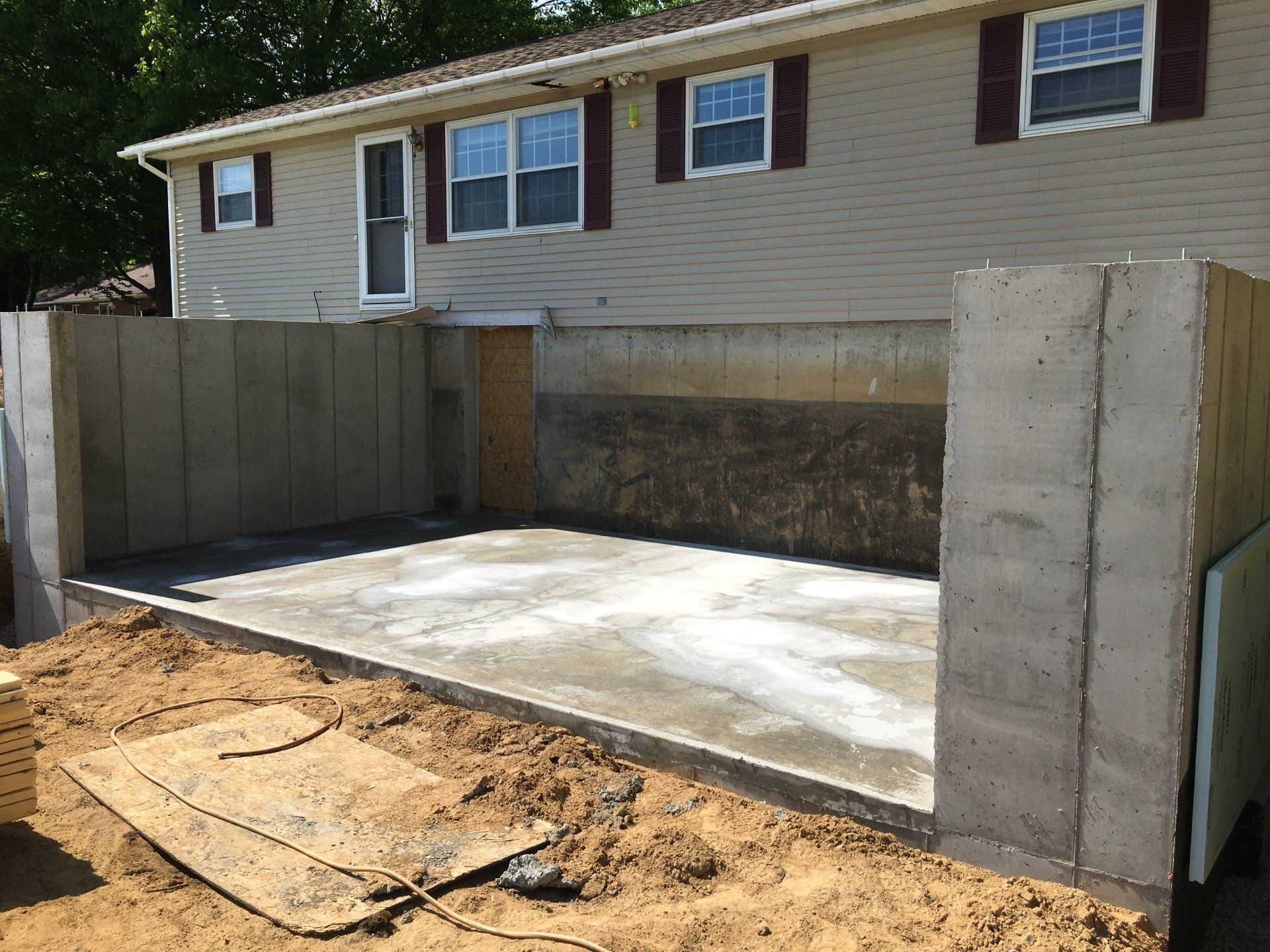 Concrete wheelchair ramp under construction beside a house with retaining walls and dirt foreground