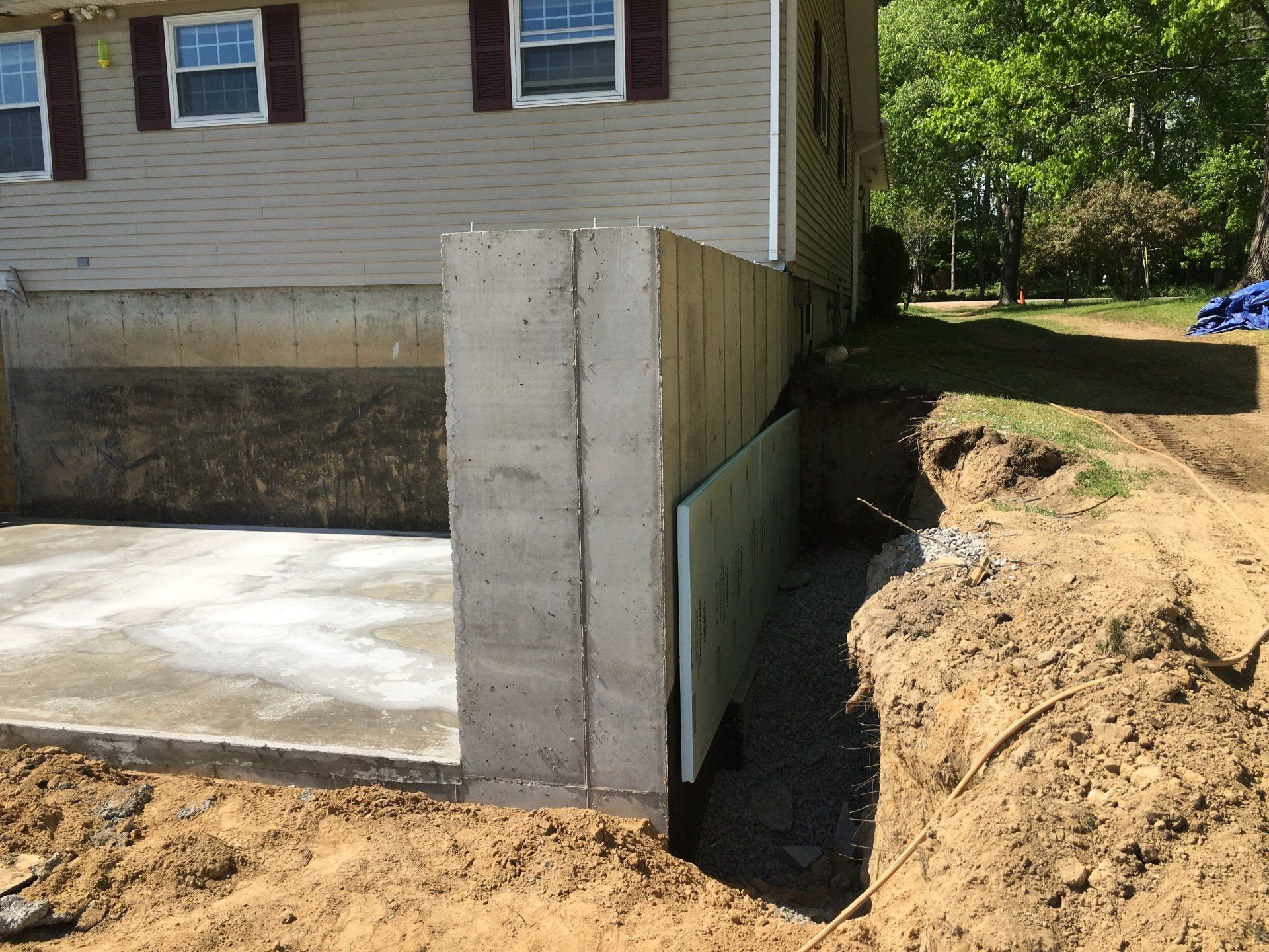 Concrete foundation wall beside a house under construction, with dirt excavation along the side