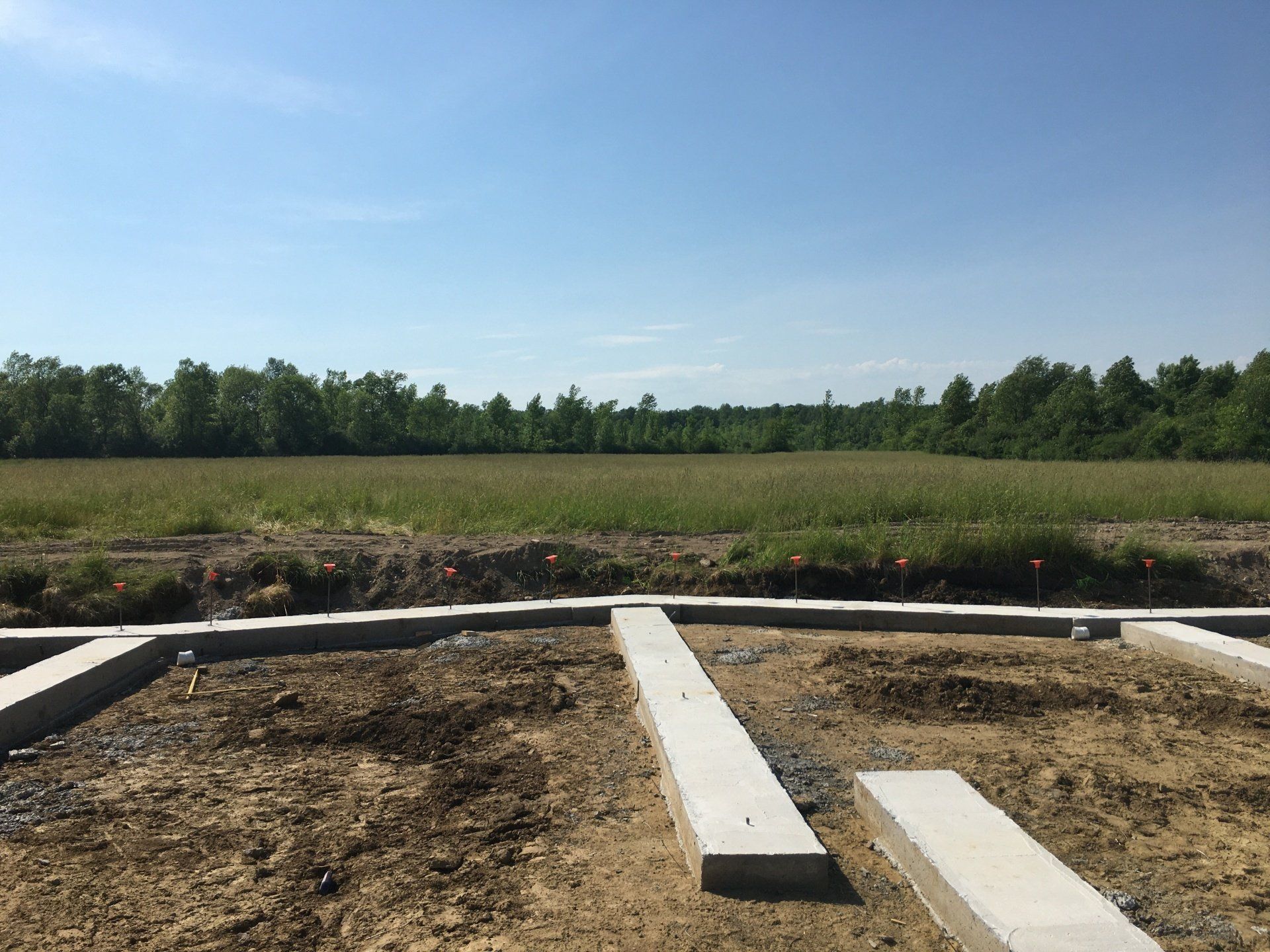 Concrete foundation slabs in a dirt lot with trees and open sky in the background