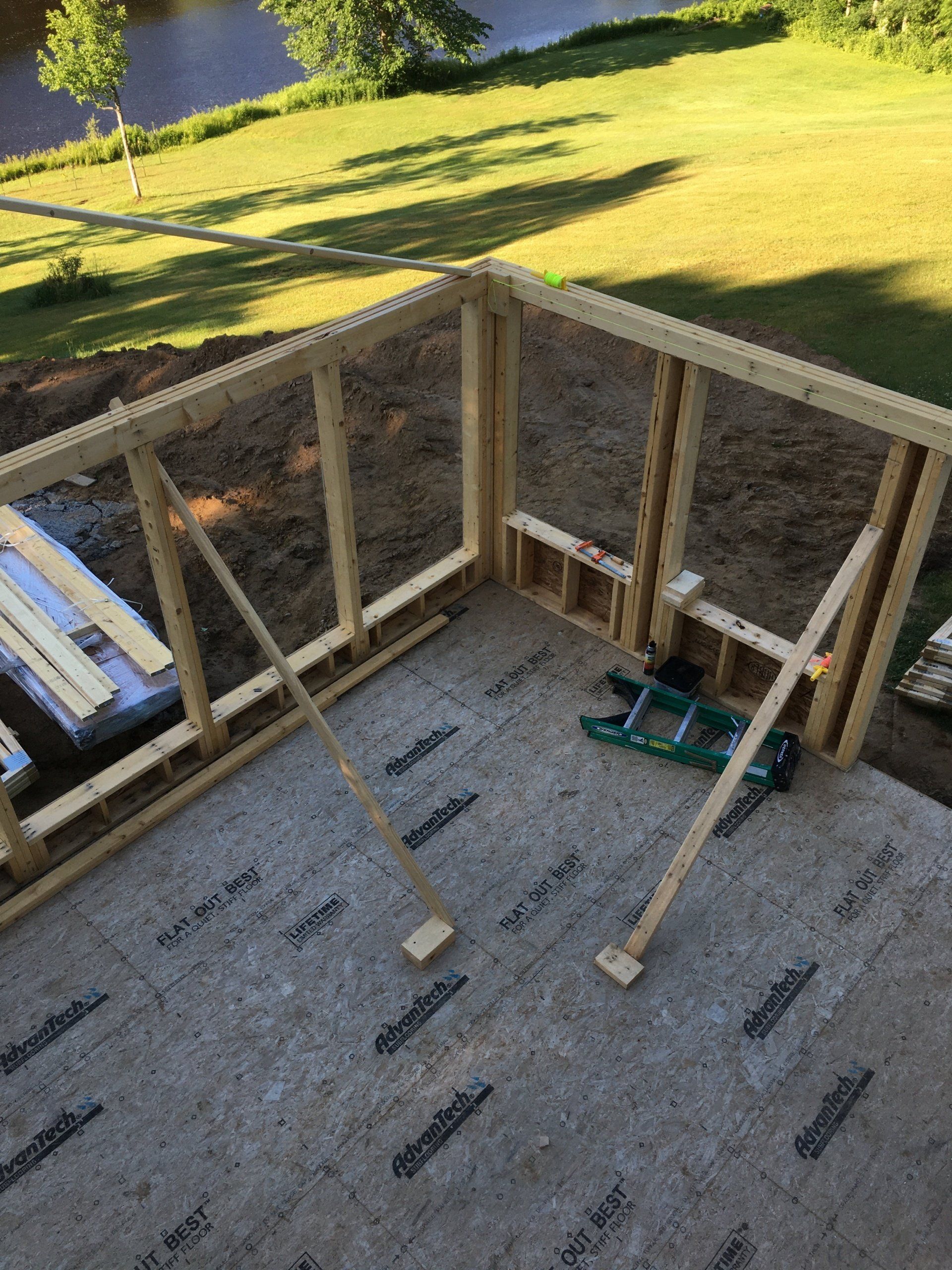 Wood-framed deck under construction with concrete floor, tools, and sunny backyard beyond the railing.