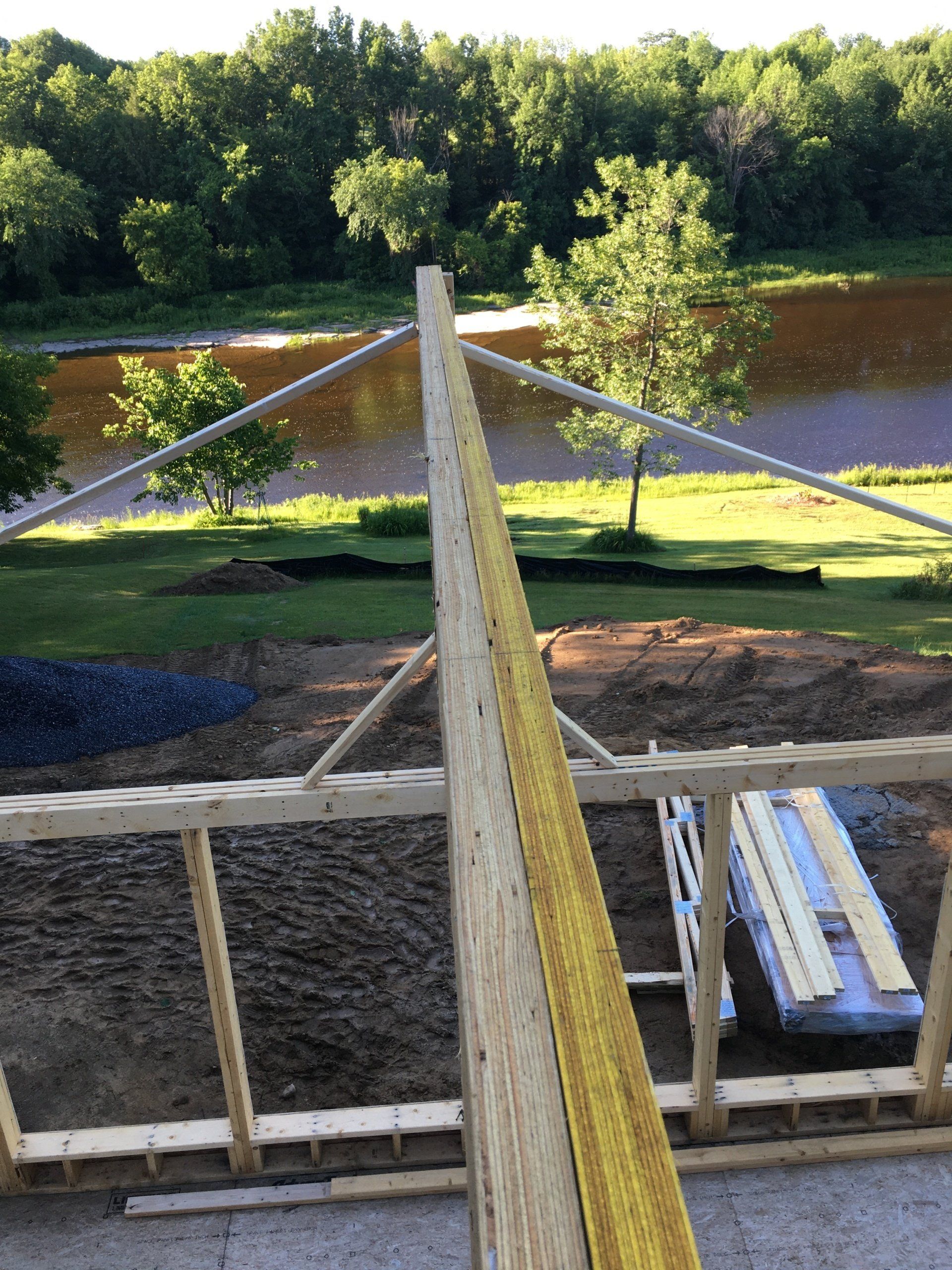 Wooden construction site with central beam and diagonal supports beside a riverbank and trees