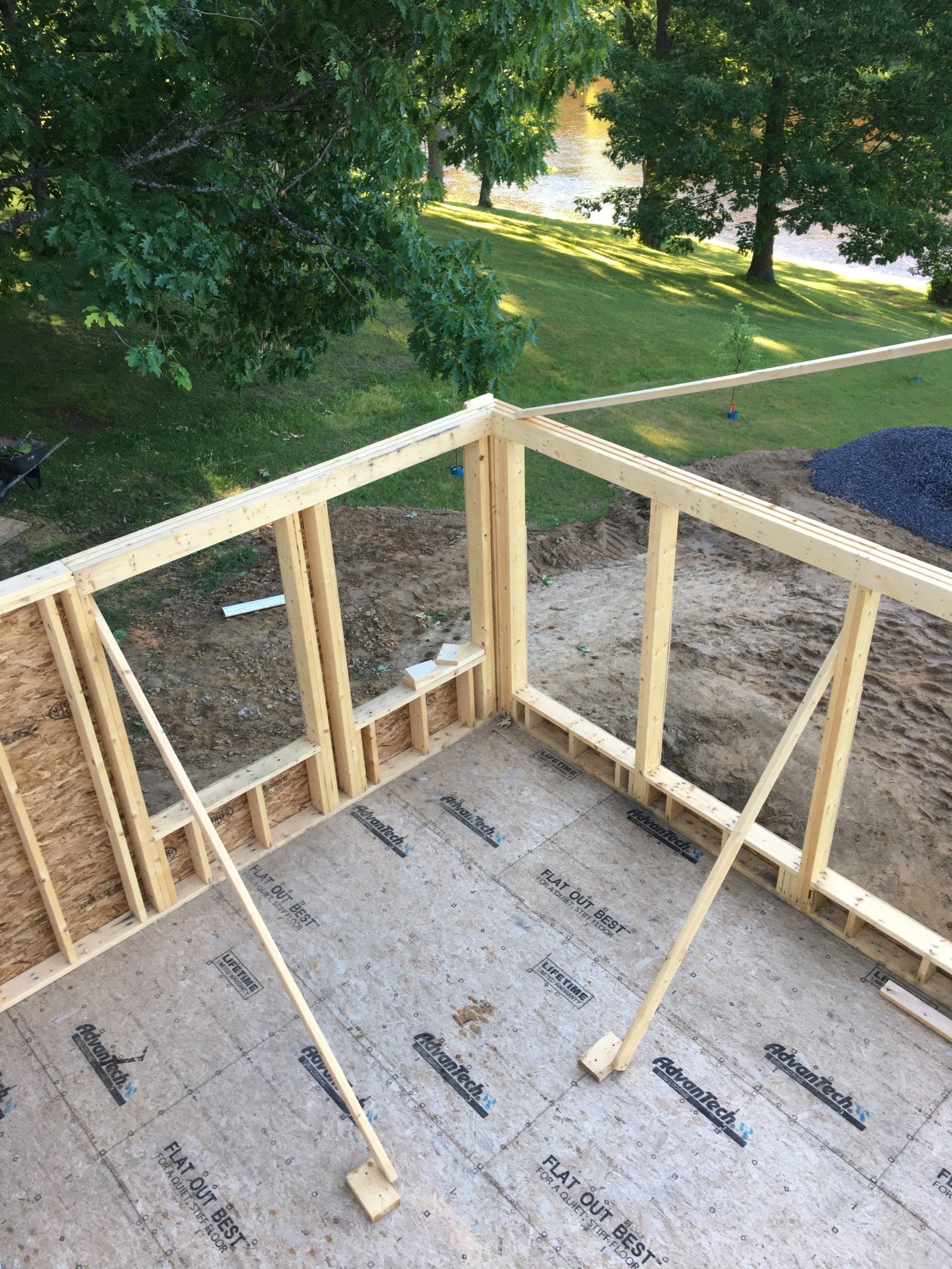 Wood-framed house deck under construction with plywood floor and wooded yard beyond