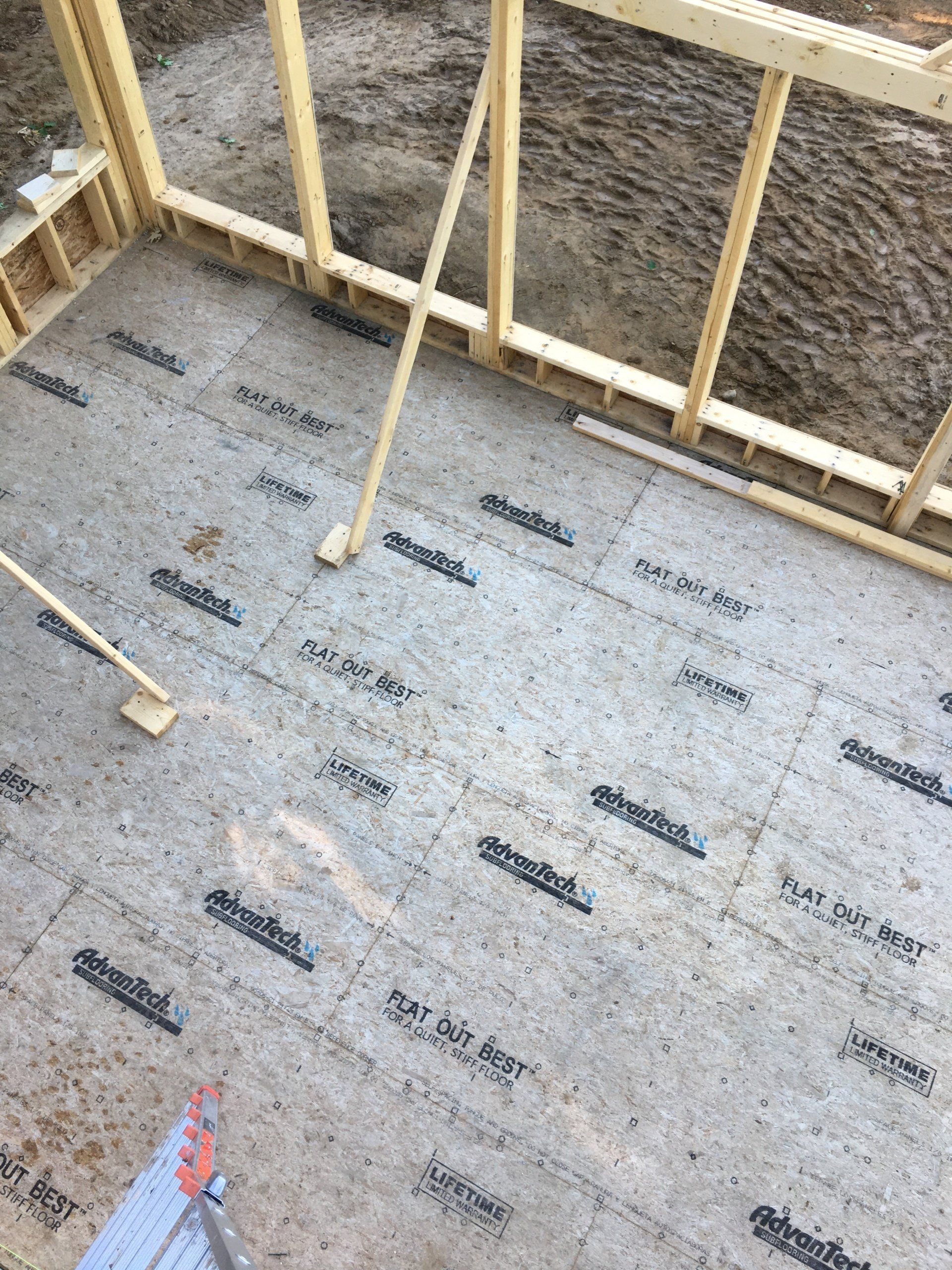 Construction site floor framed with insulation board and exposed wooden wall studs.