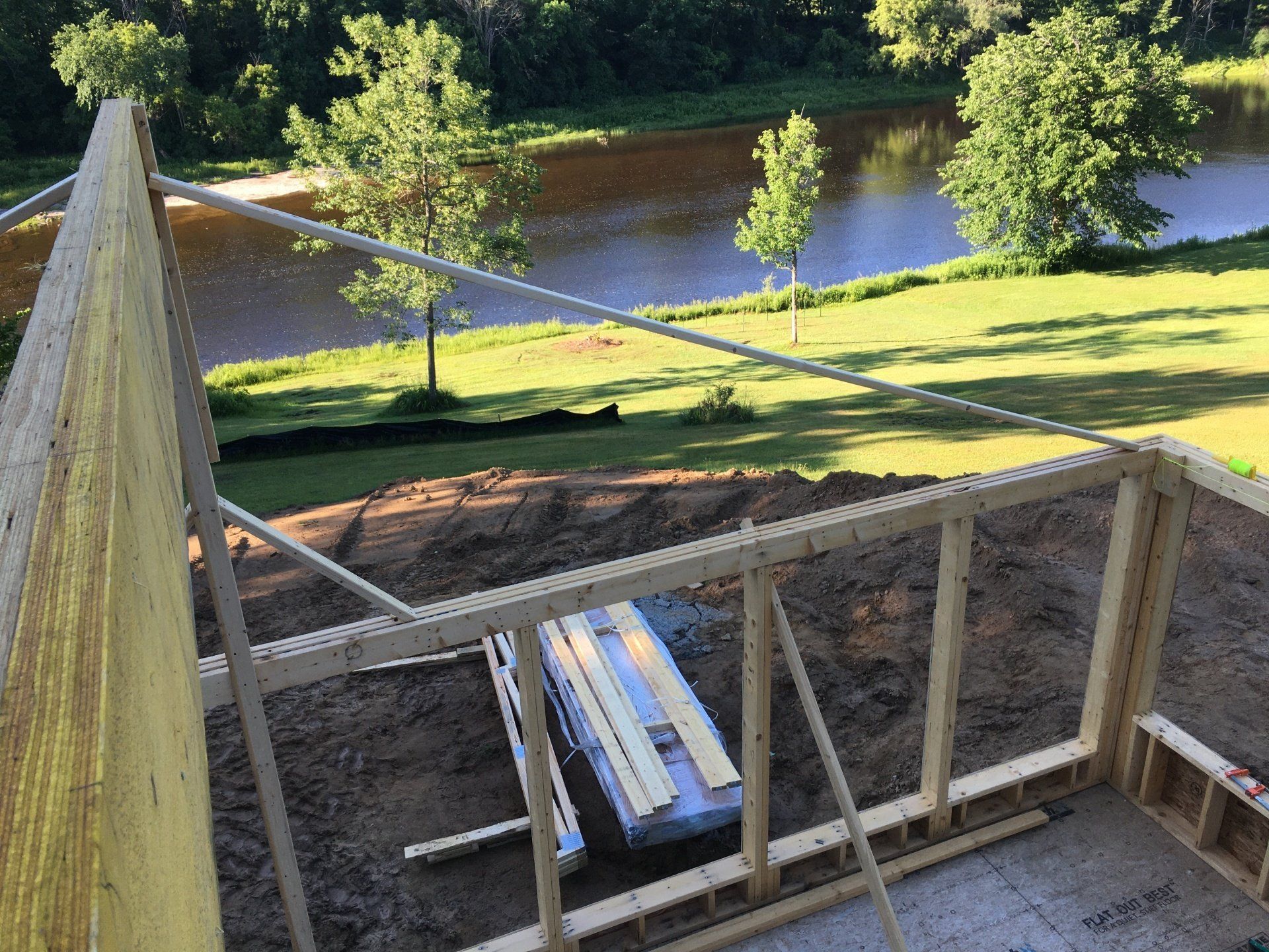 Construction site with wooden framing and stacked lumber beside a river on a sunny day