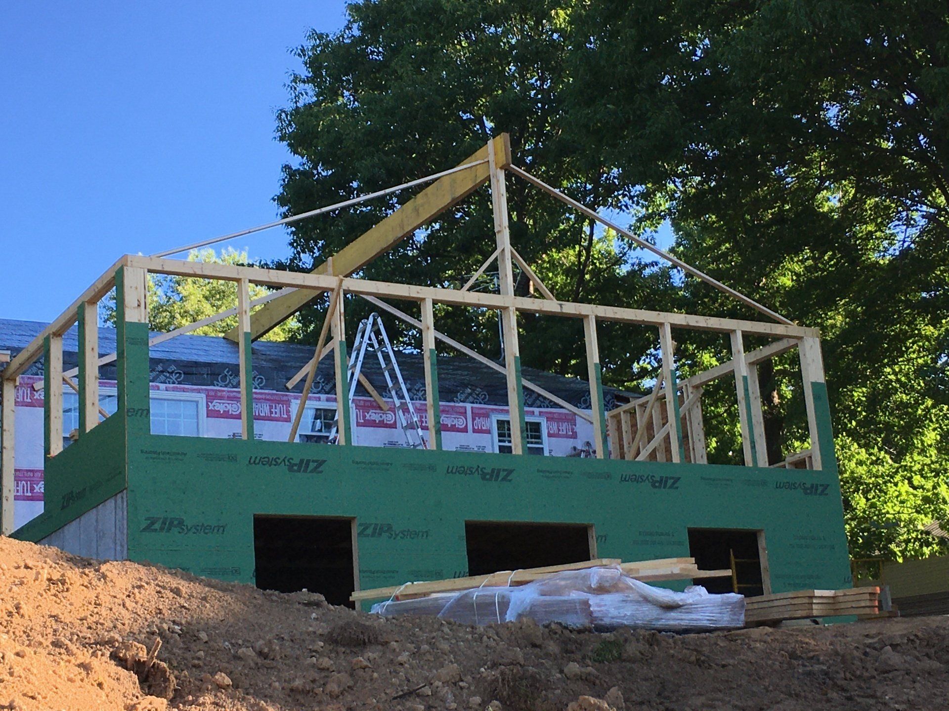 Partially built house frame with green sheathing and exposed wood beams on a sunny site