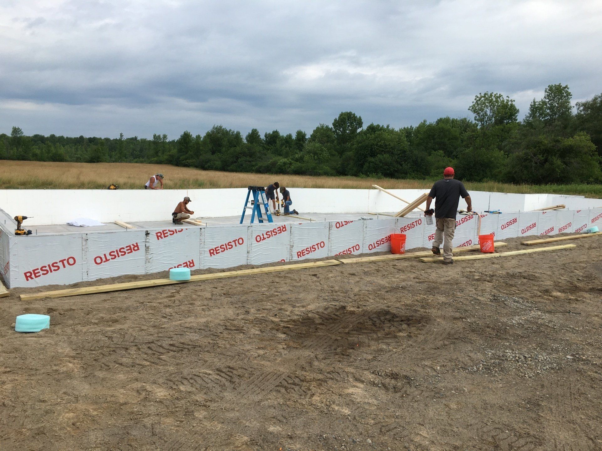 Workers installing a white barrier at a muddy outdoor dirt track beside a pond