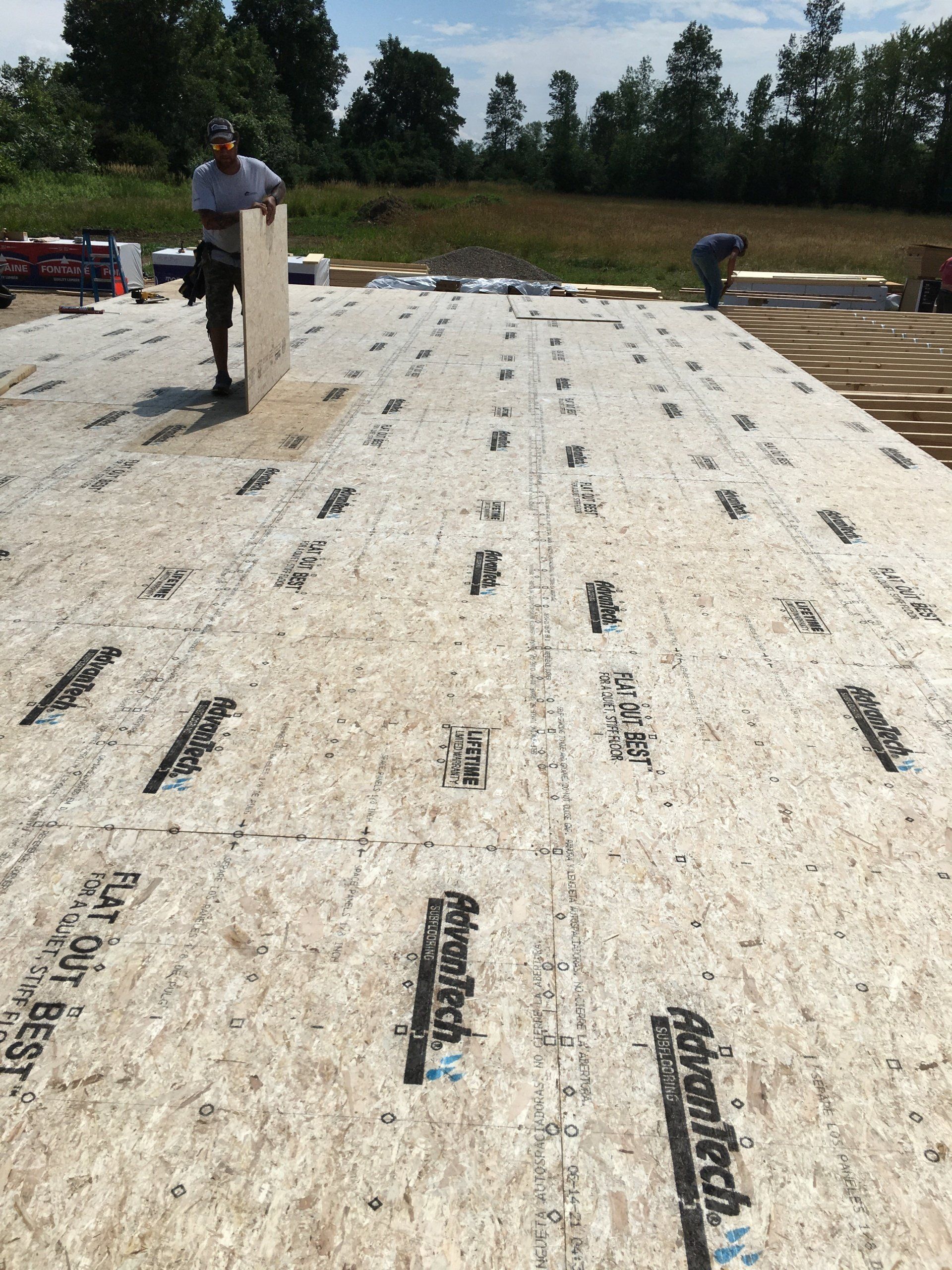 Workers installing white roofing underlayment on a large roof, with tools and materials spread across the surface.