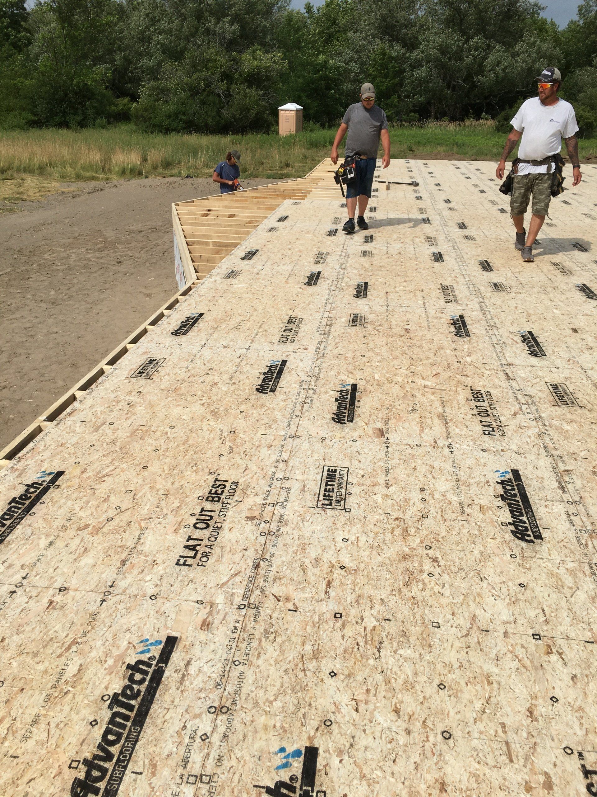 Two workers on an OSB subfloor under construction outdoors