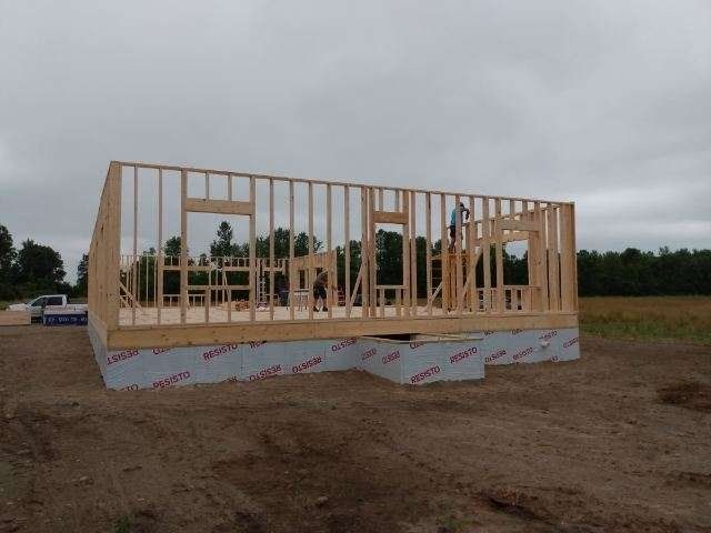 Framed house under construction on a bare lot beneath a cloudy sky