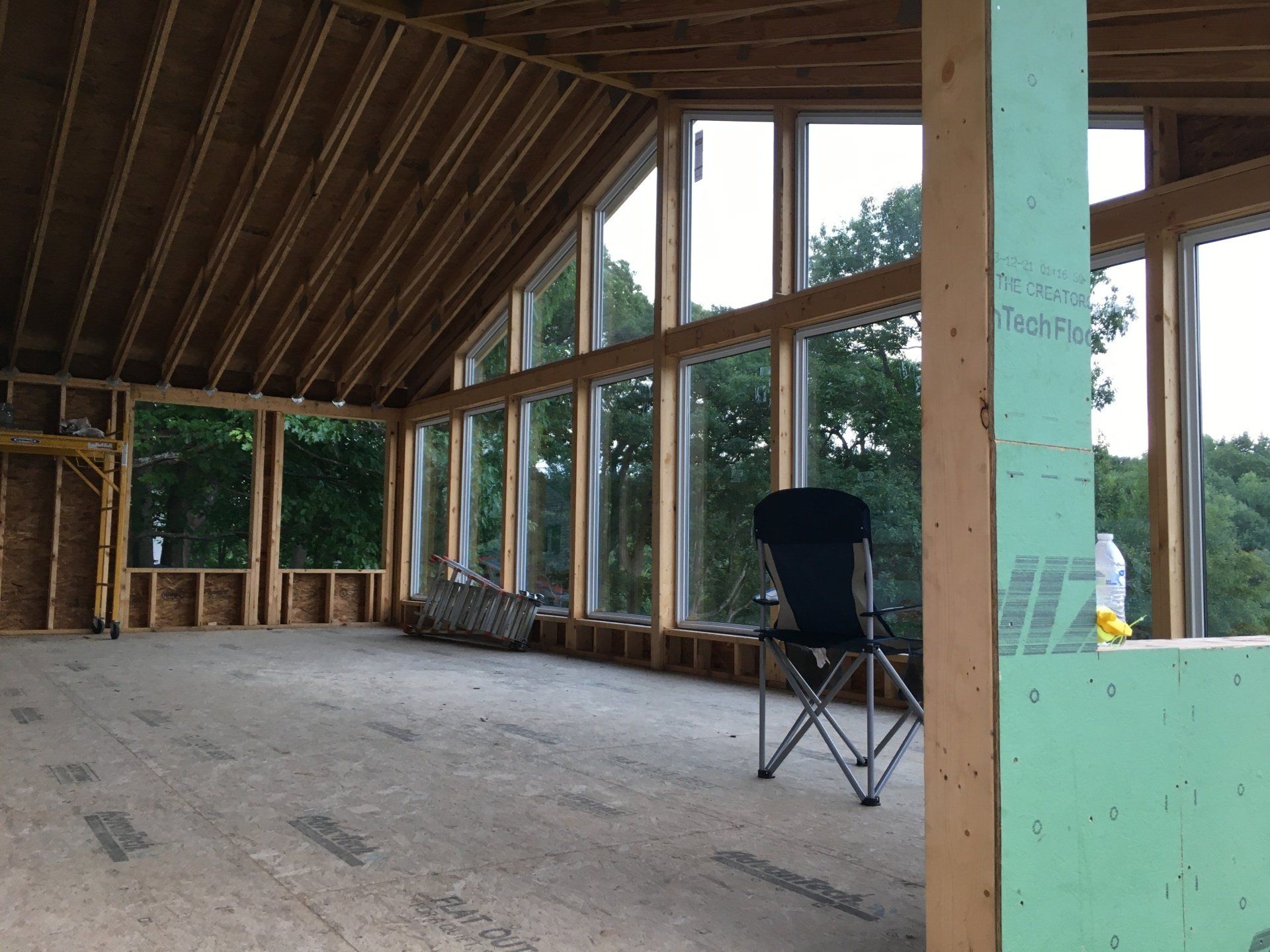 Partially finished wooden room with large windows, exposed beams, and a folding chair on the floor