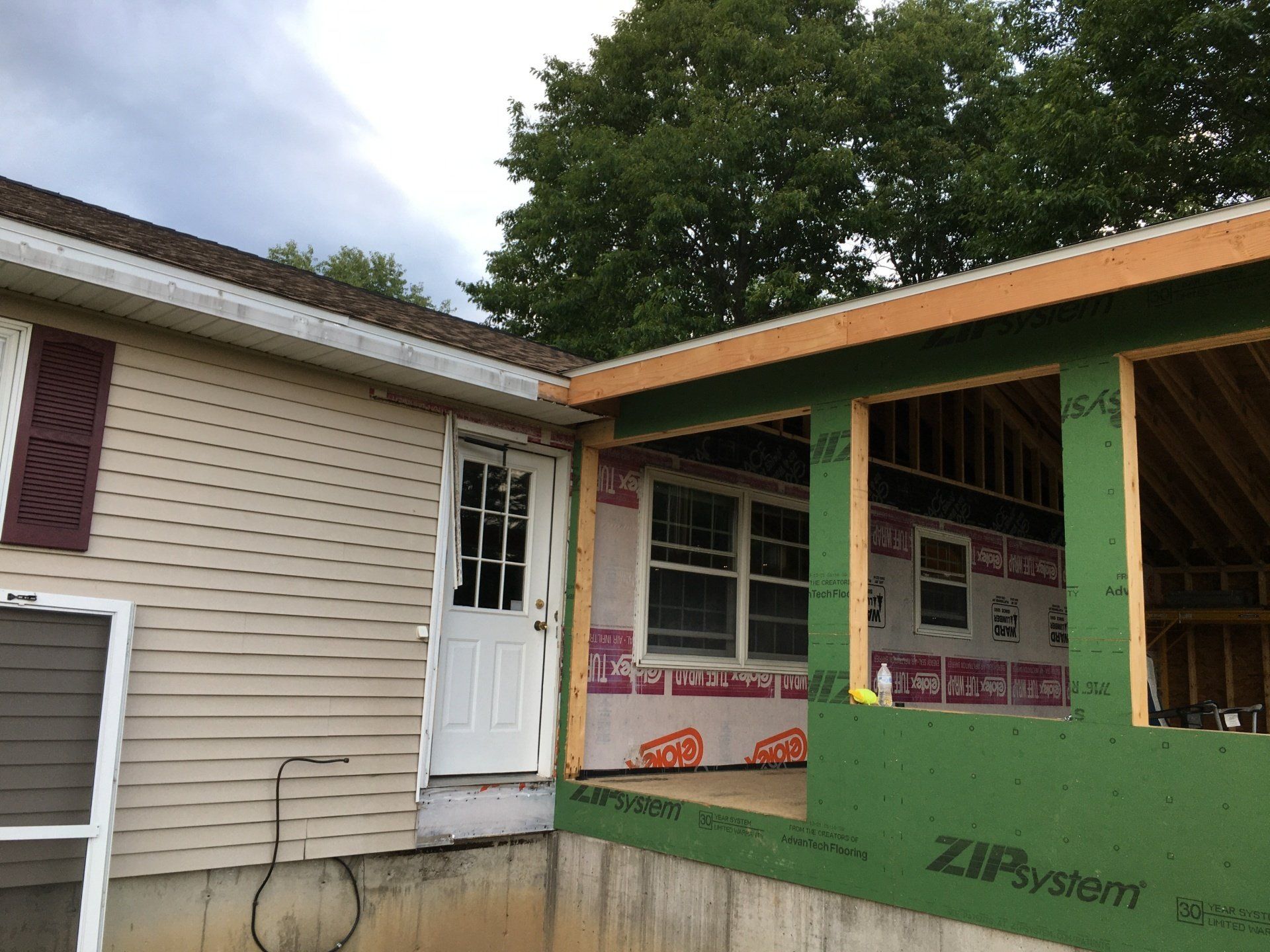 Partially built house addition with green and orange trim beside a beige home