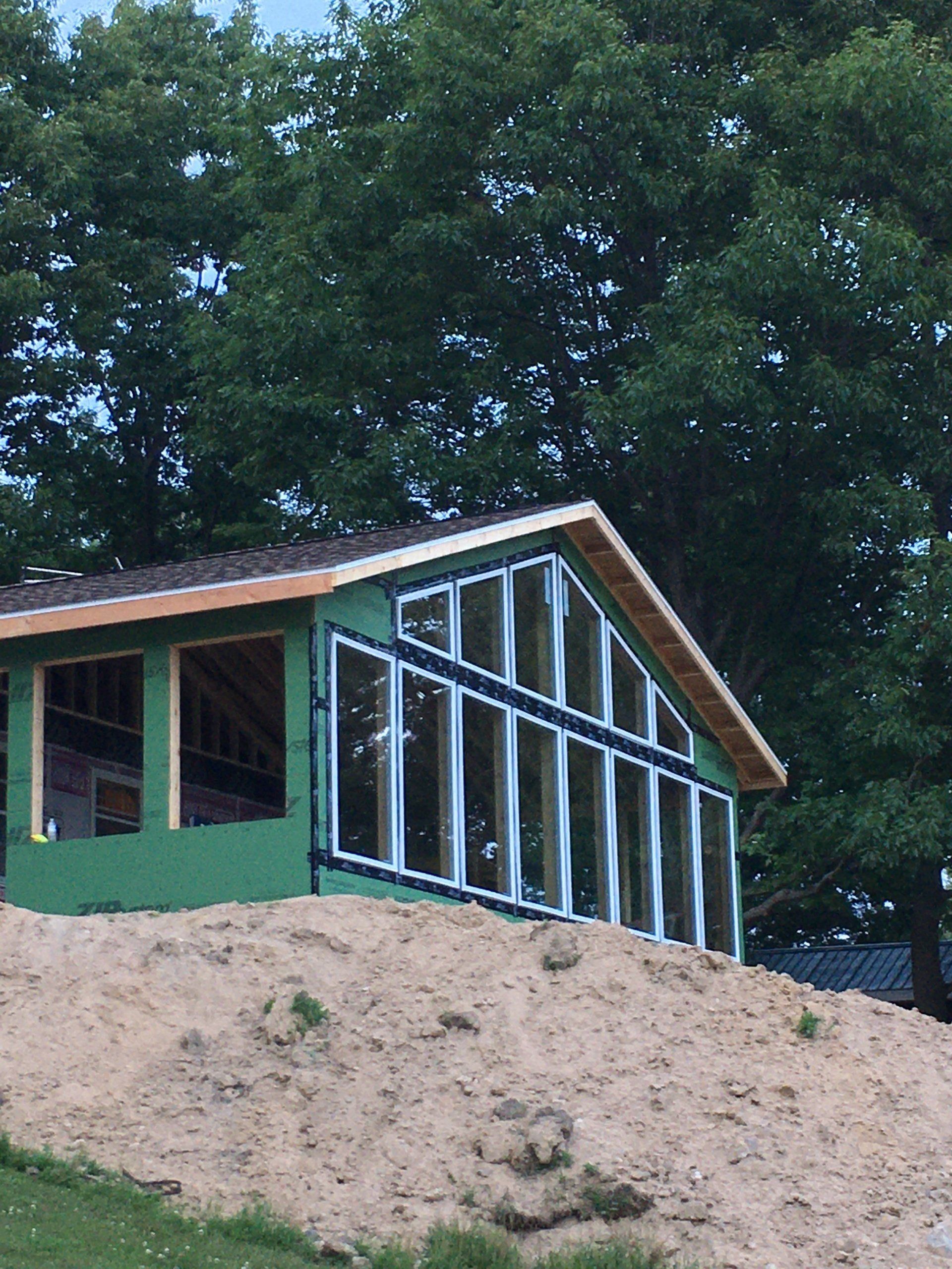 Green house under construction on a sandy slope with tall trees in the background