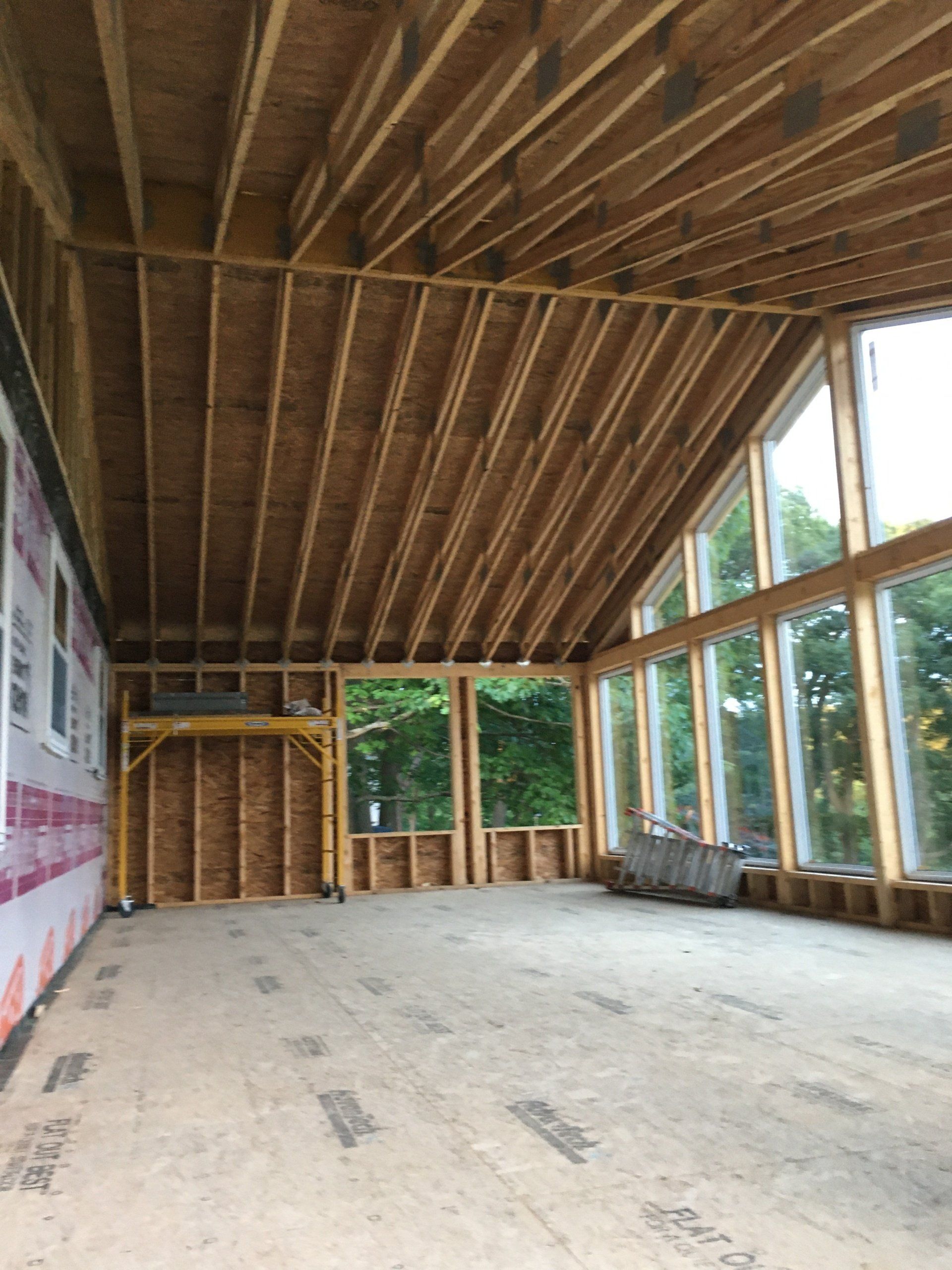 Empty unfinished room with exposed wood framing, large windows, and a concrete floor