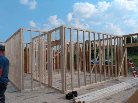 Wood-framed house under construction with exposed studs and a ladder on the right under a blue sky