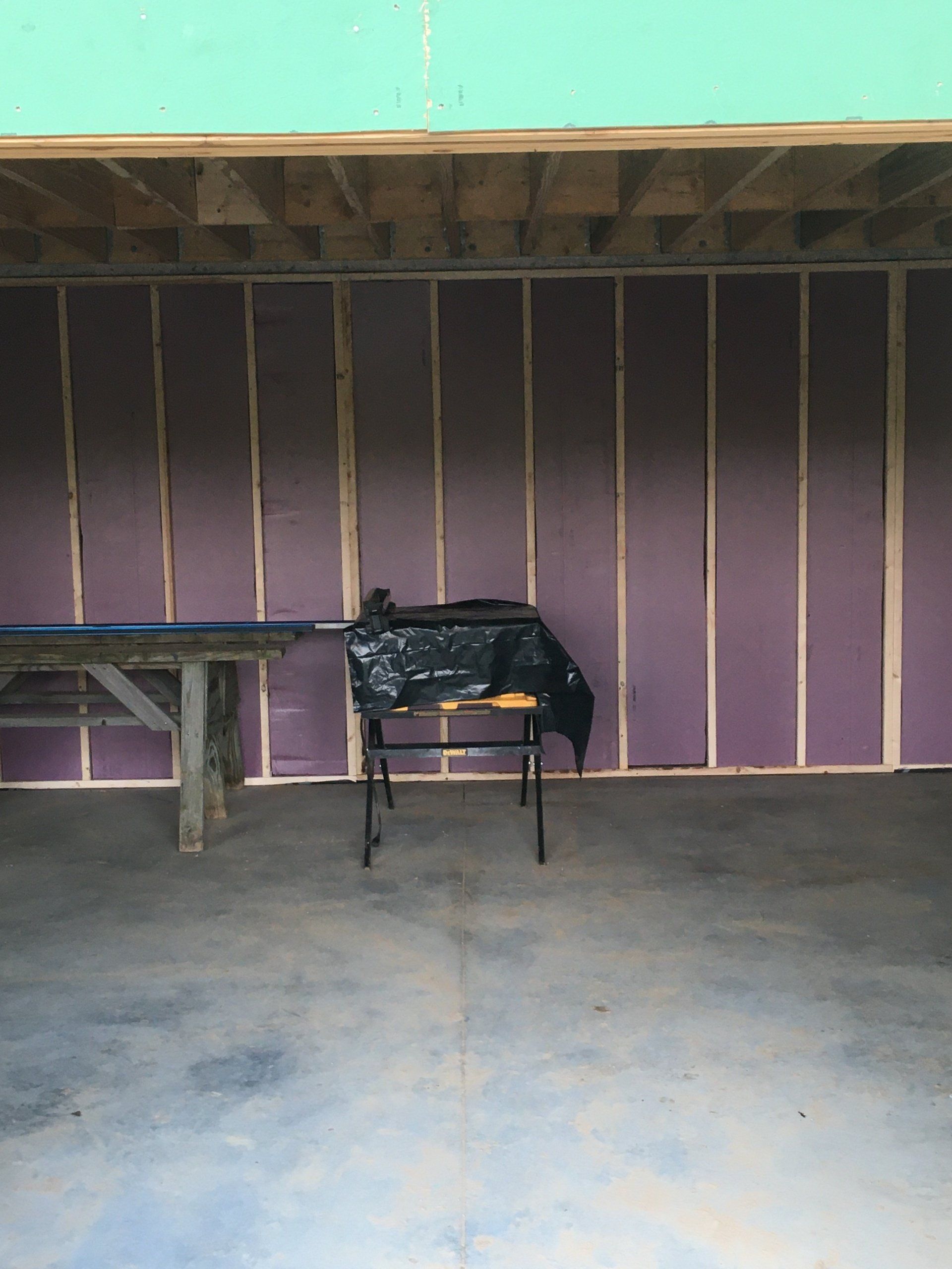 Basement with unfinished purple walls, exposed beams, and a folding table and chair on a concrete floor