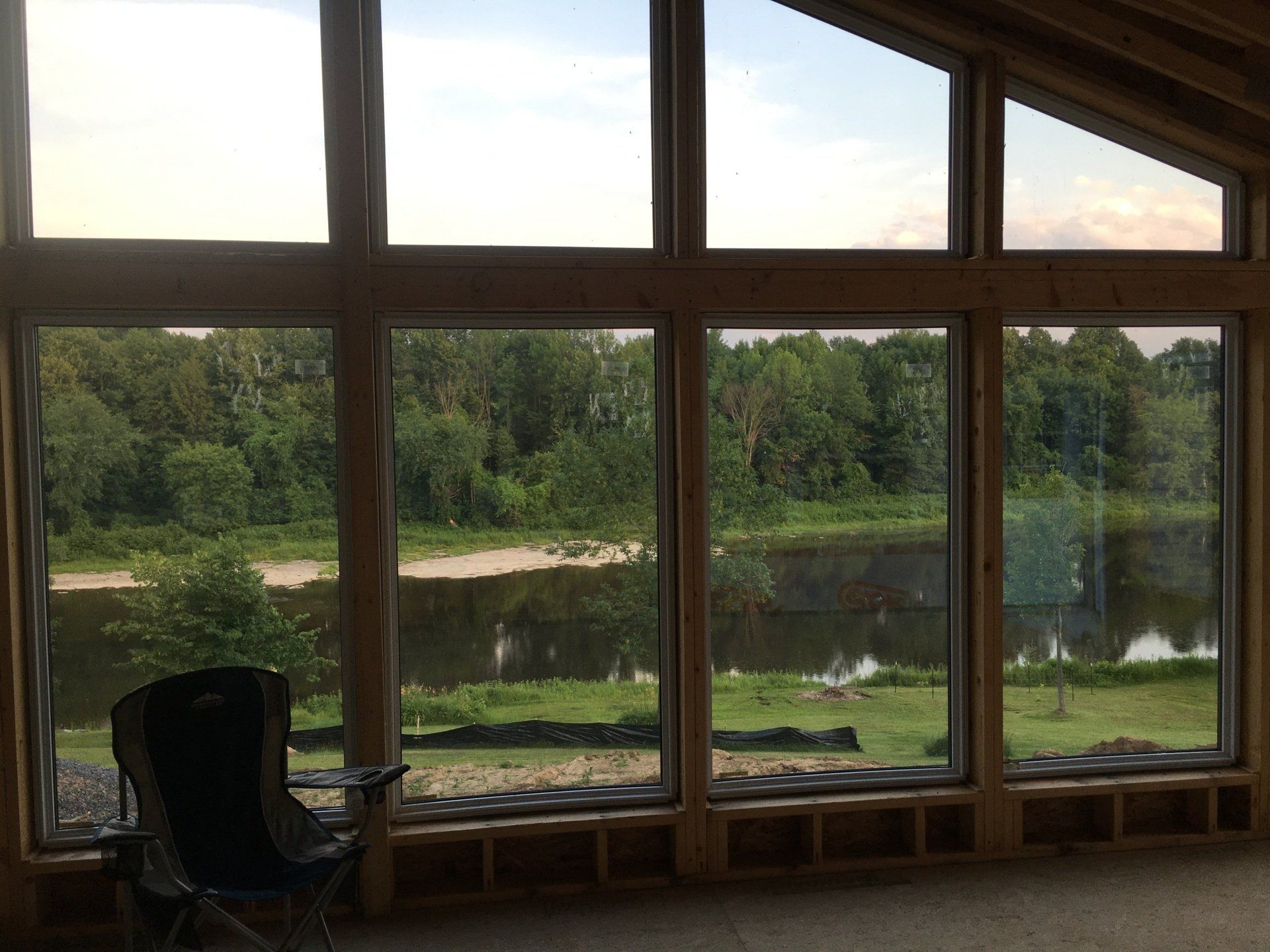 Large window overlooking a calm river and green trees, with a dark chair in the foreground
