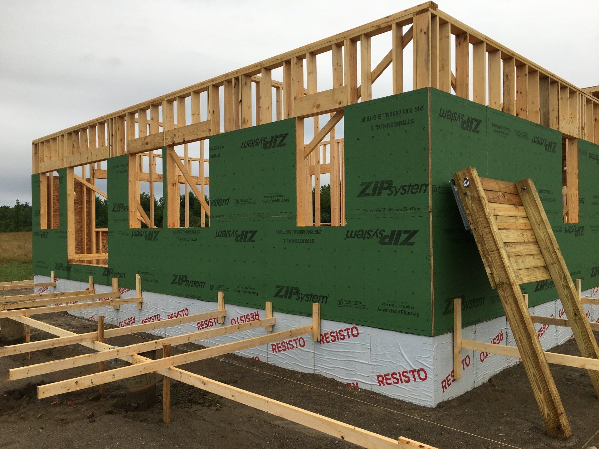 Partially framed house under construction with green house wrap and exposed wood framing