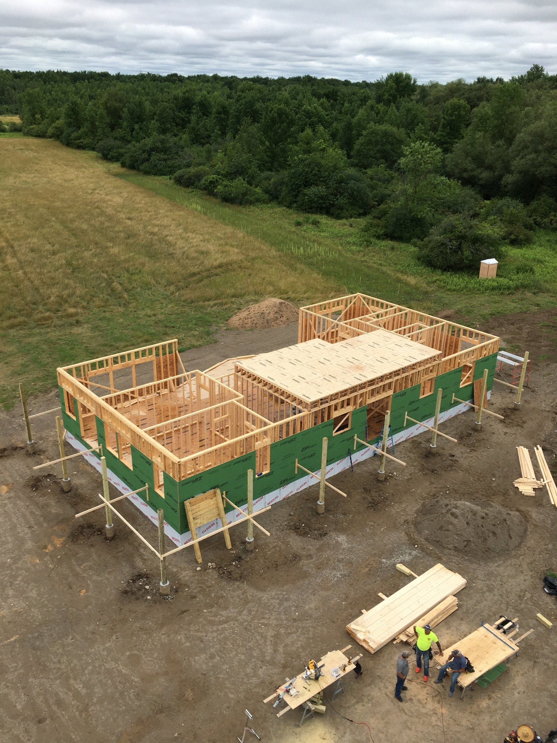 Framed house under construction on a dirt lot, with workers and building materials nearby.