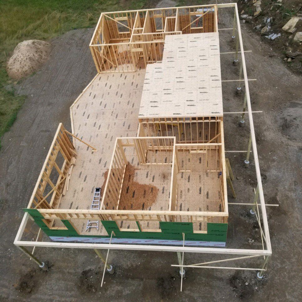 Aerial view of a wooden house frame under construction on a gravel lot.
