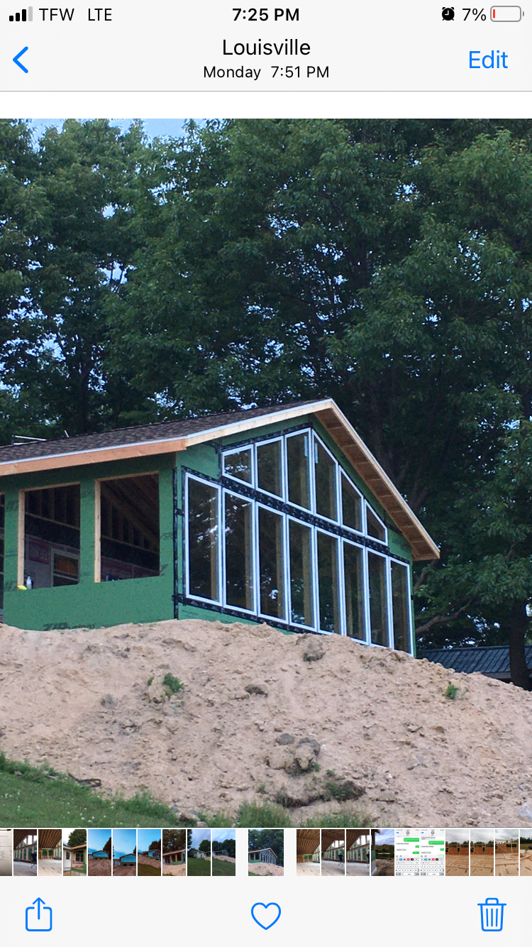 Small green cabin under construction on a sandy hillside, with exposed framing and trees behind it.