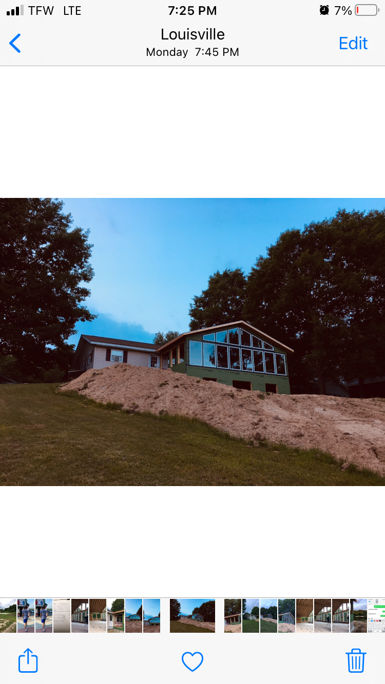 Blue house on a grassy hill with trees on both sides and a pile of dirt in front