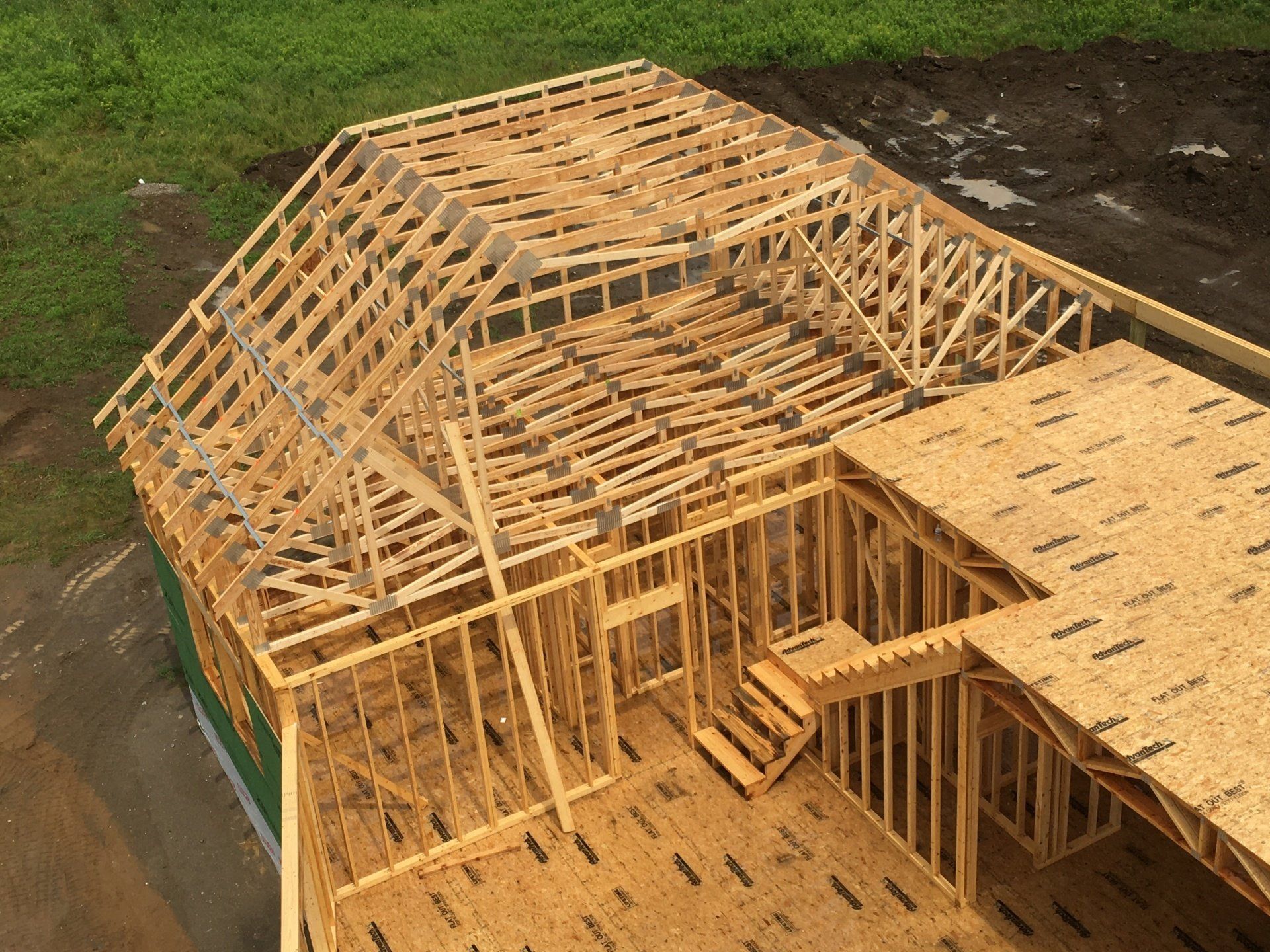 Wooden house framing under construction with exposed roof trusses and plywood decking.
