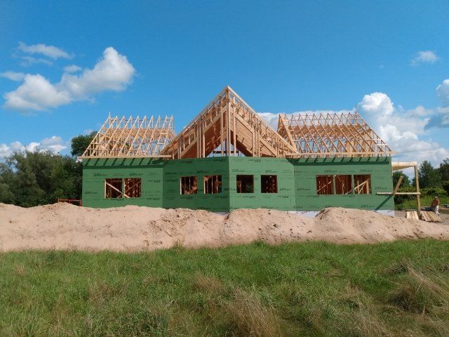 Partially built house with green exterior walls and exposed wooden roof framing under a blue sky