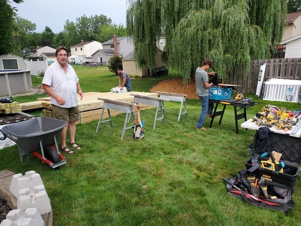 People setting up and grilling food at a backyard cookout with tables and tools on a grassy lawn.