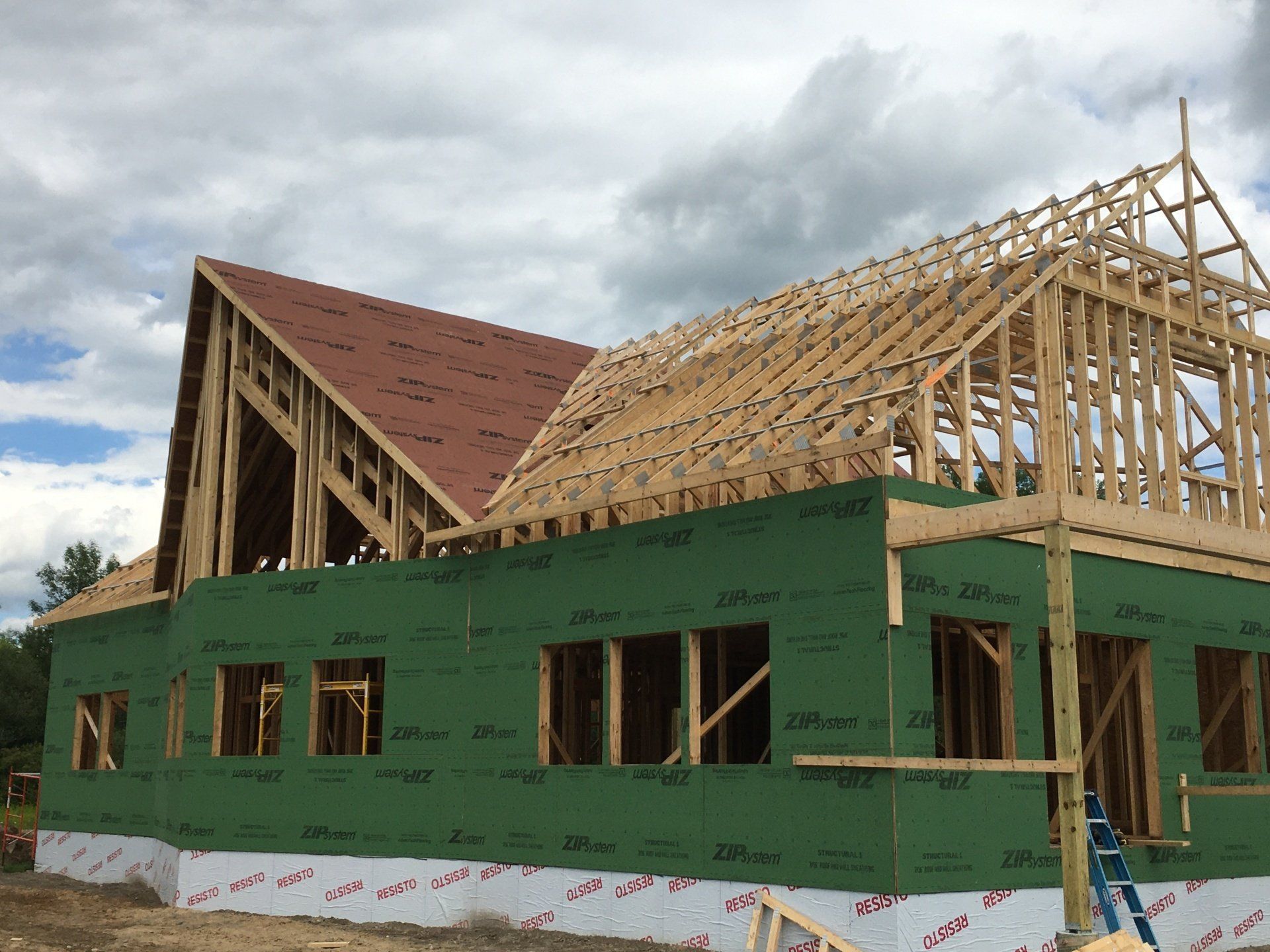 House under construction with green wrap, exposed wooden framing, and partially shingled roof