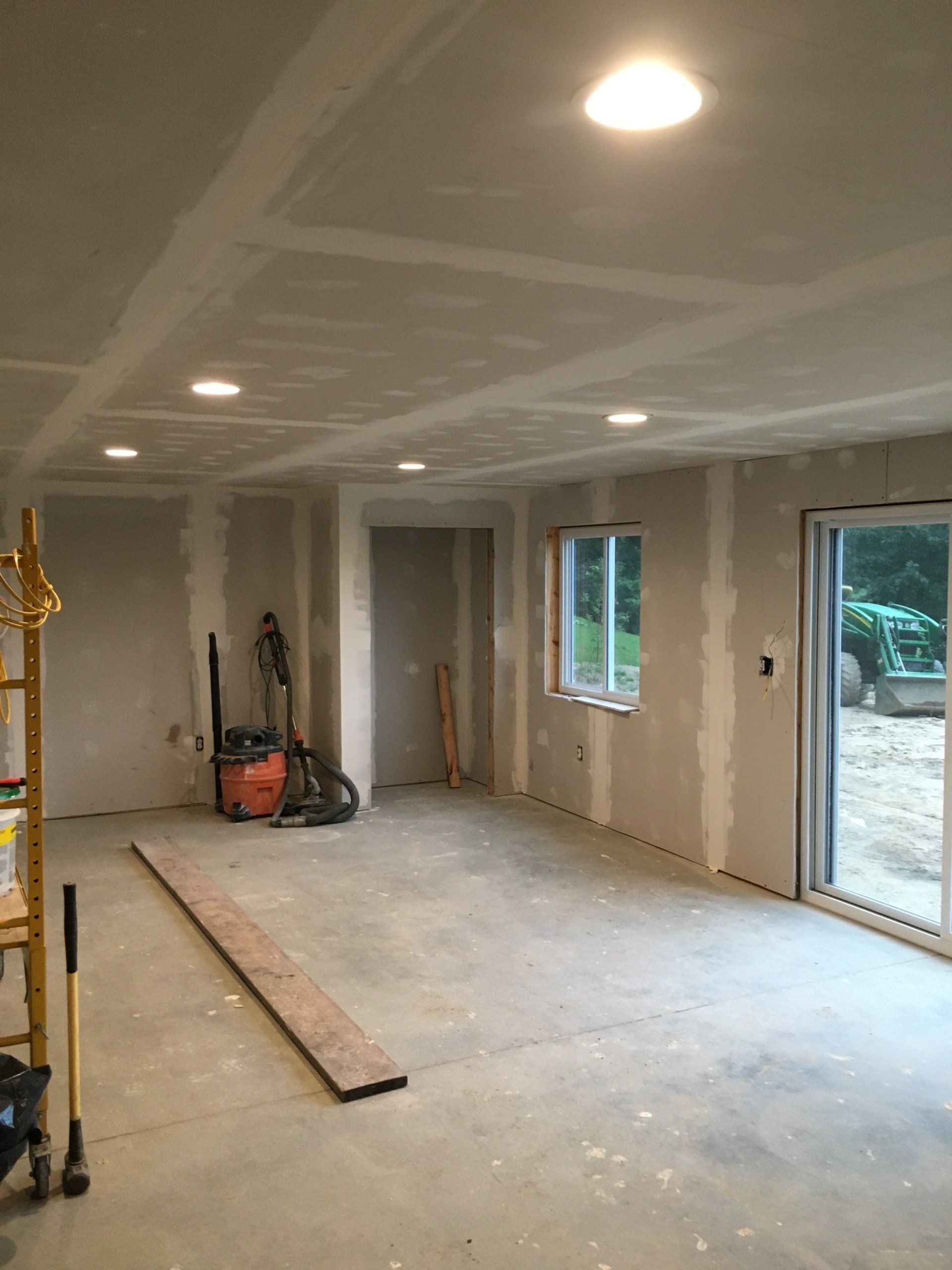 Unfinished drywall room with recessed lights, tools, and two windows beside a sliding glass door.