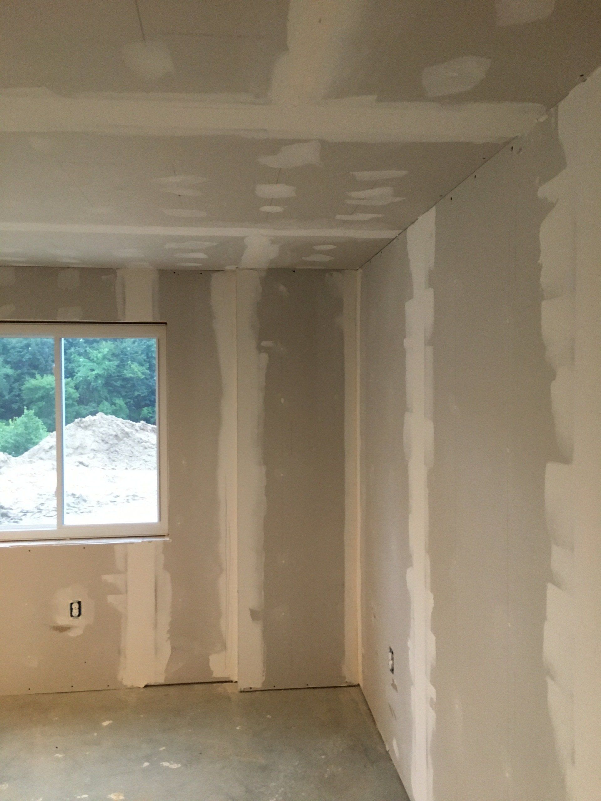 Empty room under renovation with unfinished drywall and a window overlooking trees and a roof.