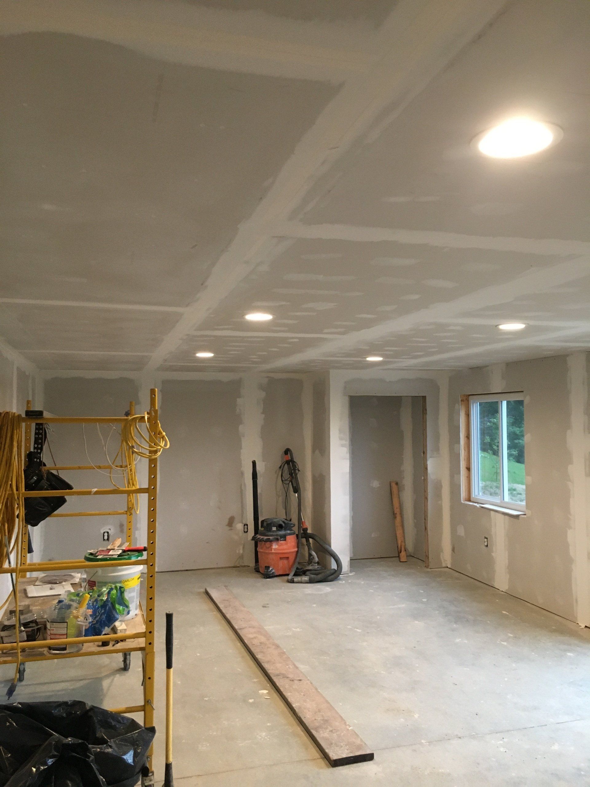 Unfinished room under renovation with drywall, ceiling lights, tools, and a ladder.