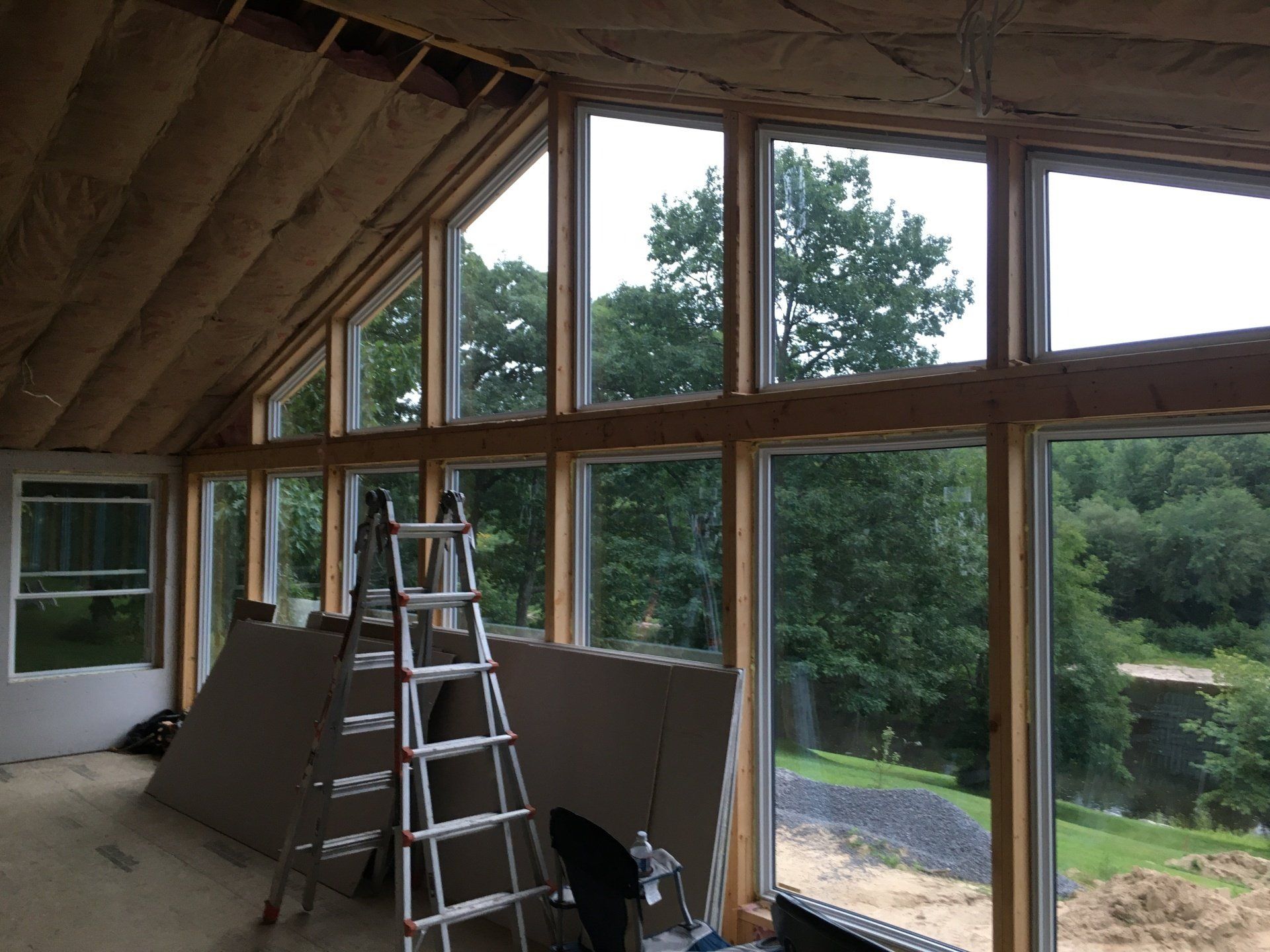 Unfinished interior with large windows, ladder, and sloped ceiling overlooking trees outside